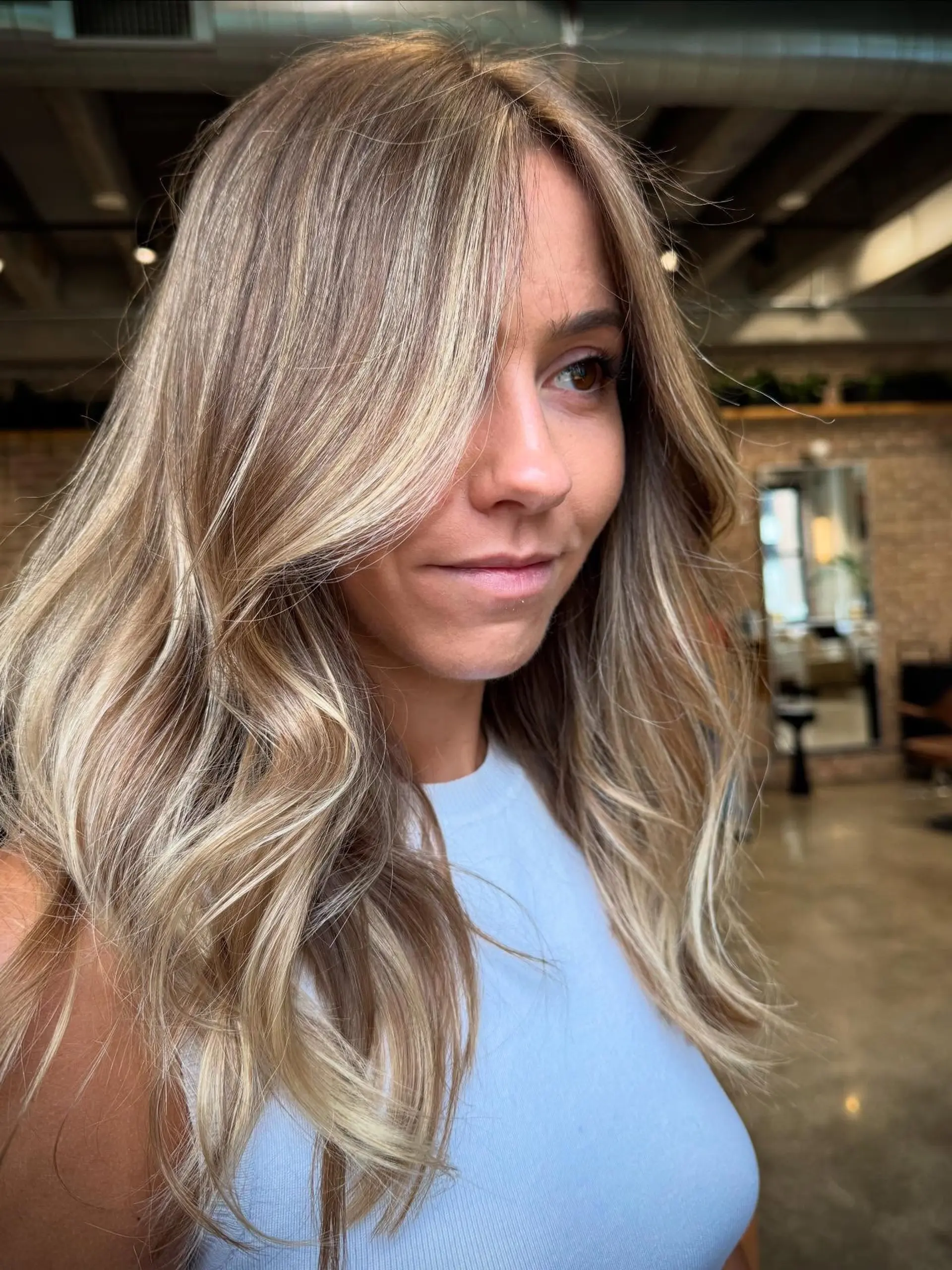 Long, flowing waves with a dimensional golden blonde foilayage, creating a sun-kissed effect with brighter face-framing highlights and subtle layering for movement. 1