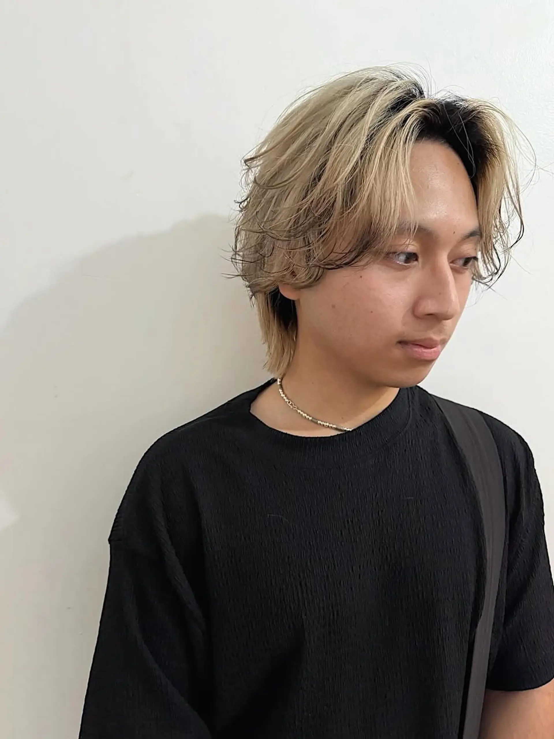 A medium-length, wavy men's flow haircut with a messy mid-part. The hair is predominantly bleached blonde with visible dark roots, creating a stylish two-tone and shadow root effect. 1