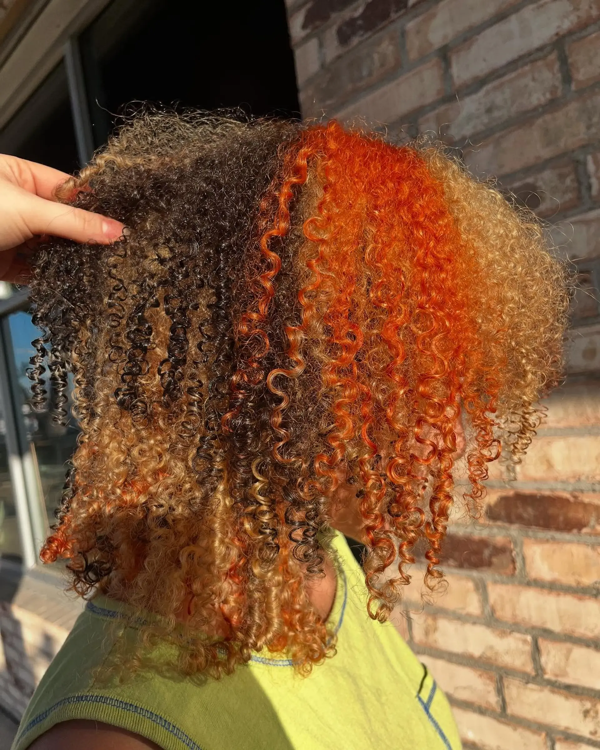 A dimensional calico color-block design featuring bold panels of vibrant orange, deep brunette, and golden blonde on curly hair. 1