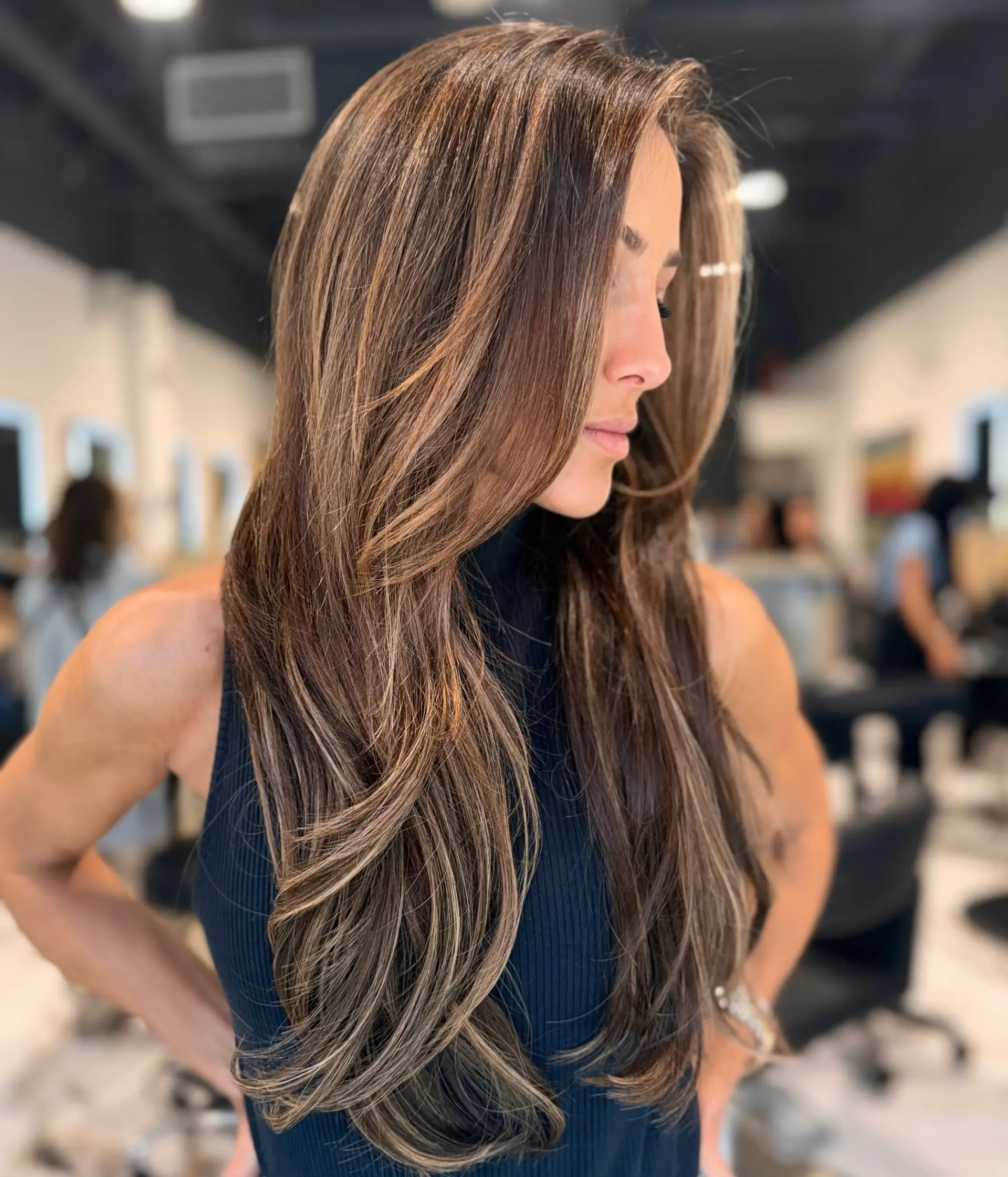 Ultra-long brunette hair enhanced with tape-in extensions, cut with soft face-framing layers and styled with gently curved ends. 1