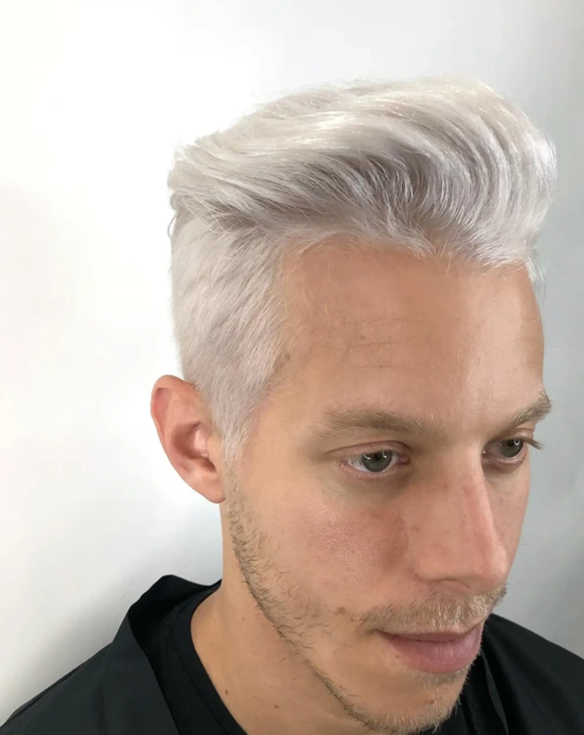 A short platinum blonde quiff with voluminous, textured top and short sides, styled in a wave-like shape.