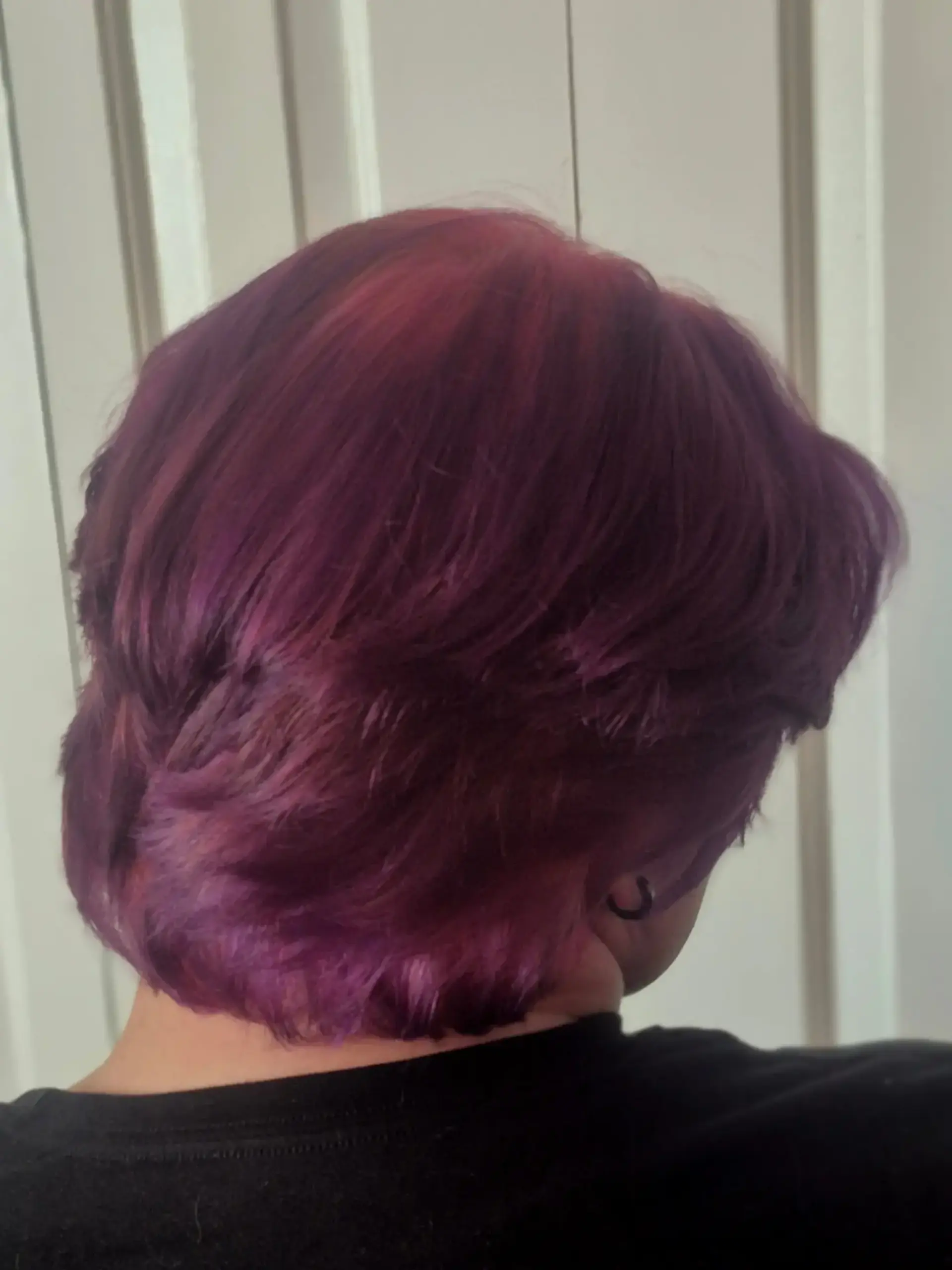 A short, textured layered haircut featuring vivid purple coloring complemented by subtle pink ghost roots. 1