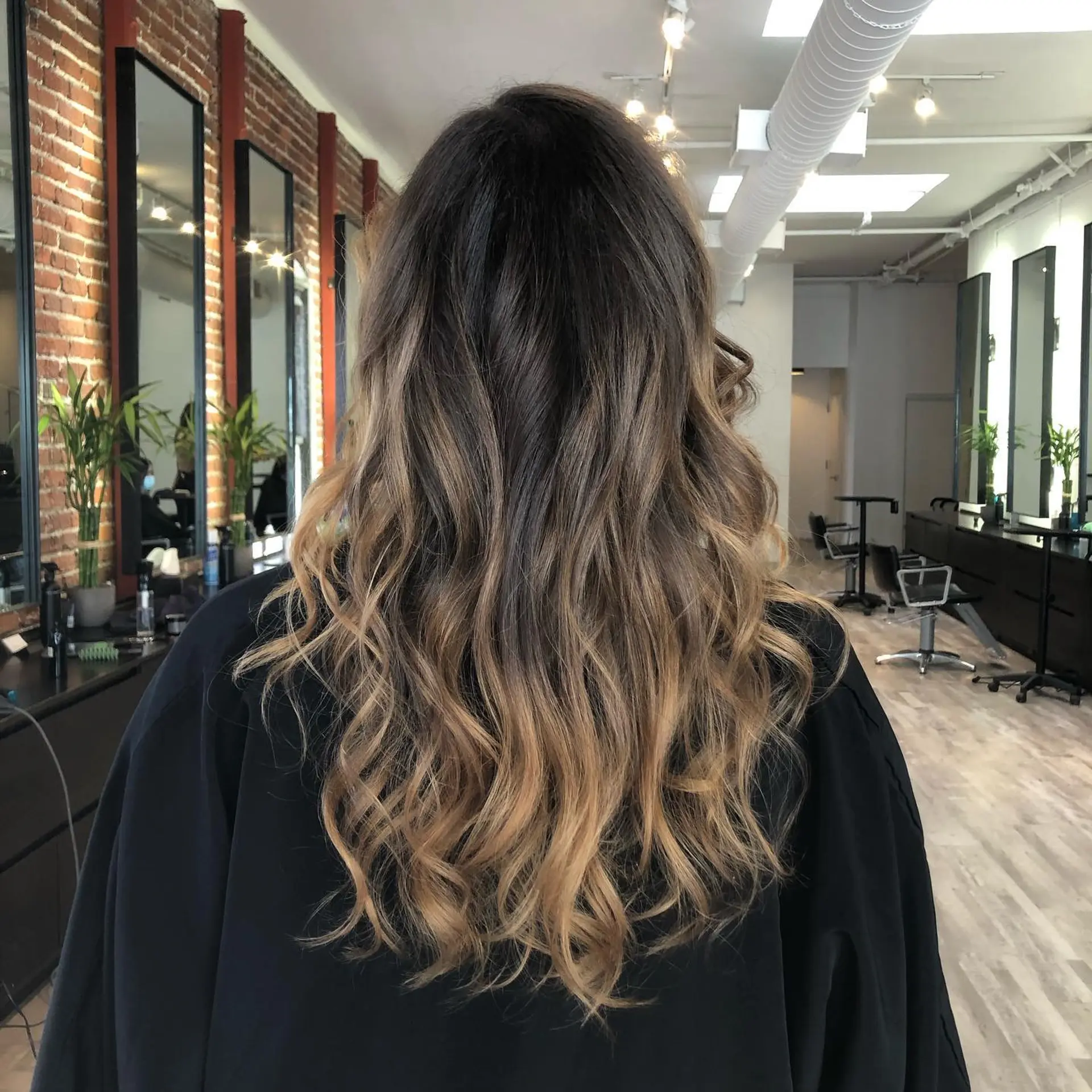 Long dark brown hair seamlessly transitioning into warm honey blonde balayage, styled in loose, textured waves. 1