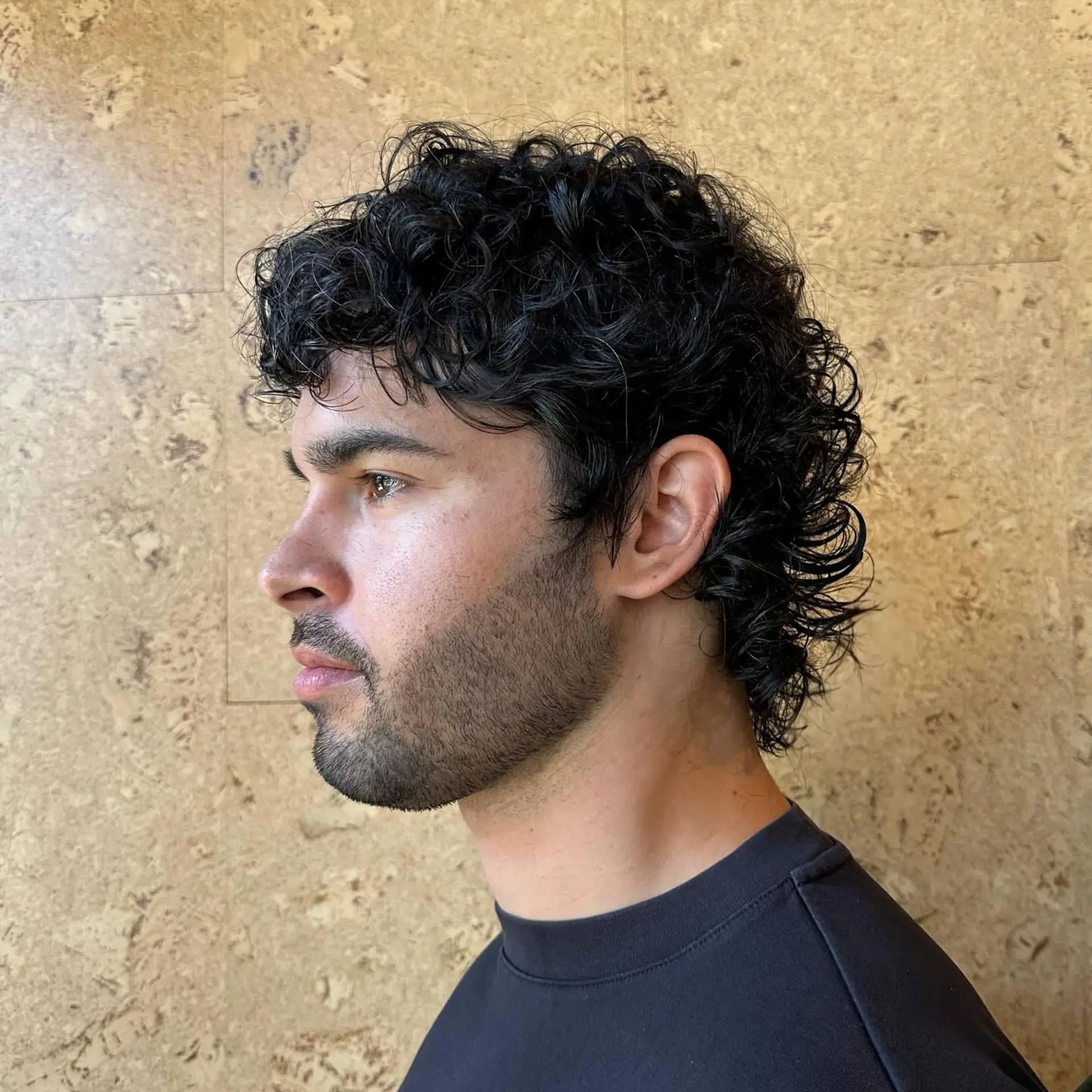 A dark curly mullet haircut featuring short curly bangs and textured curls flowing down the back of the neck. 1