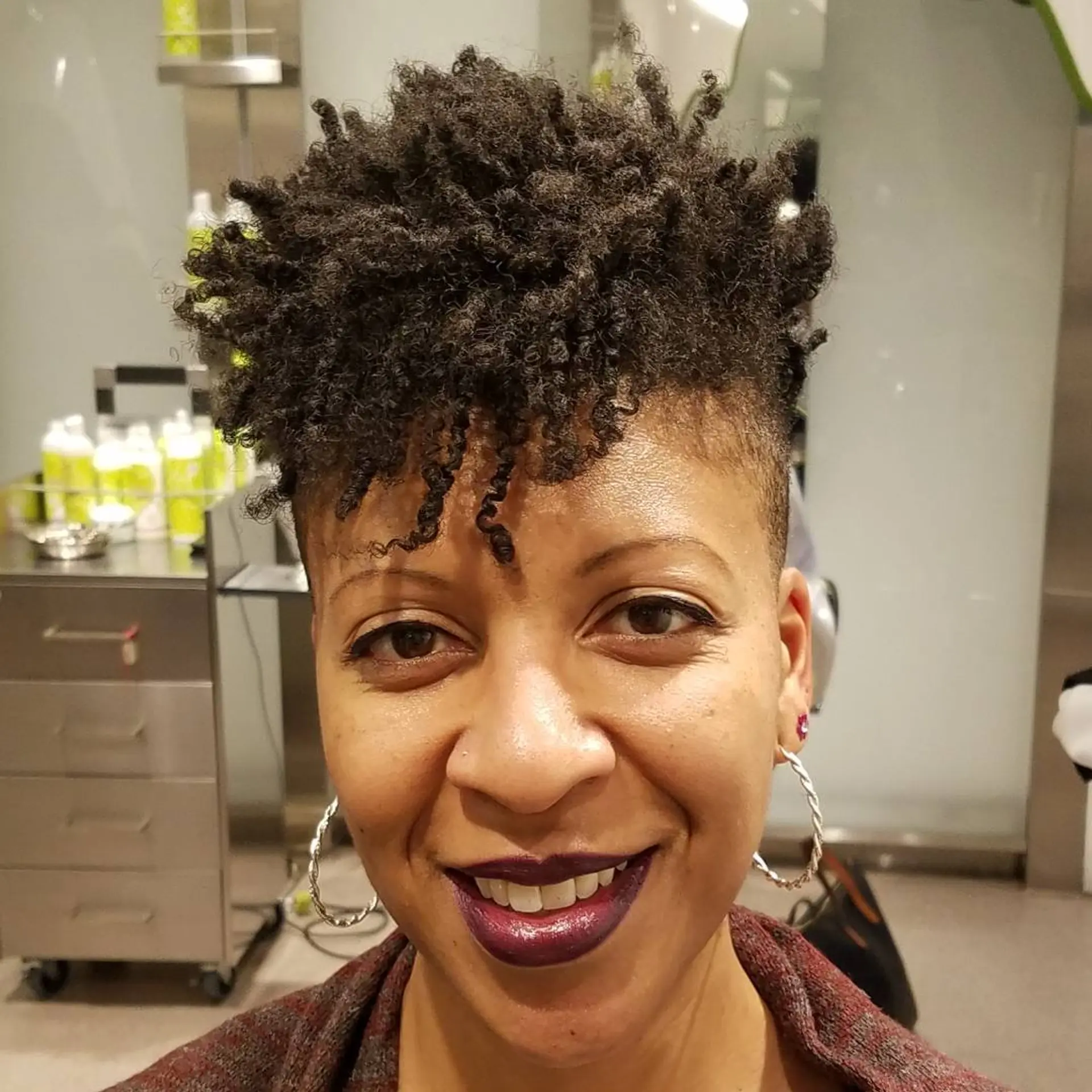 Short, coiled style with a distinct undercut on the sides and back, leaving a dense, voluminous crest of curls on top and a striking contrast between the undercut and top volume. 1