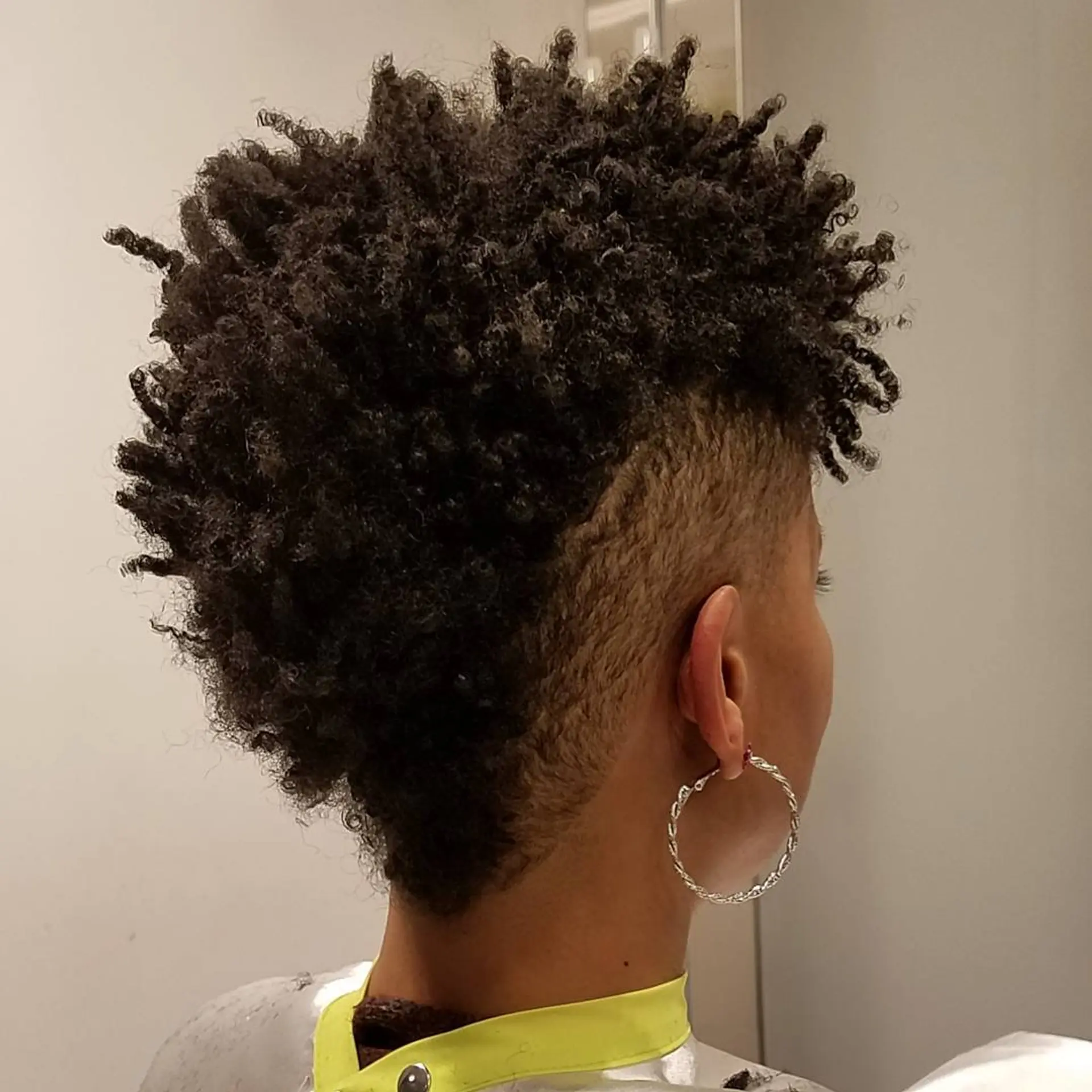 Short, coiled style with a distinct undercut on the sides and back, leaving a dense, voluminous crest of curls on top and a striking contrast between the undercut and top volume. 2
