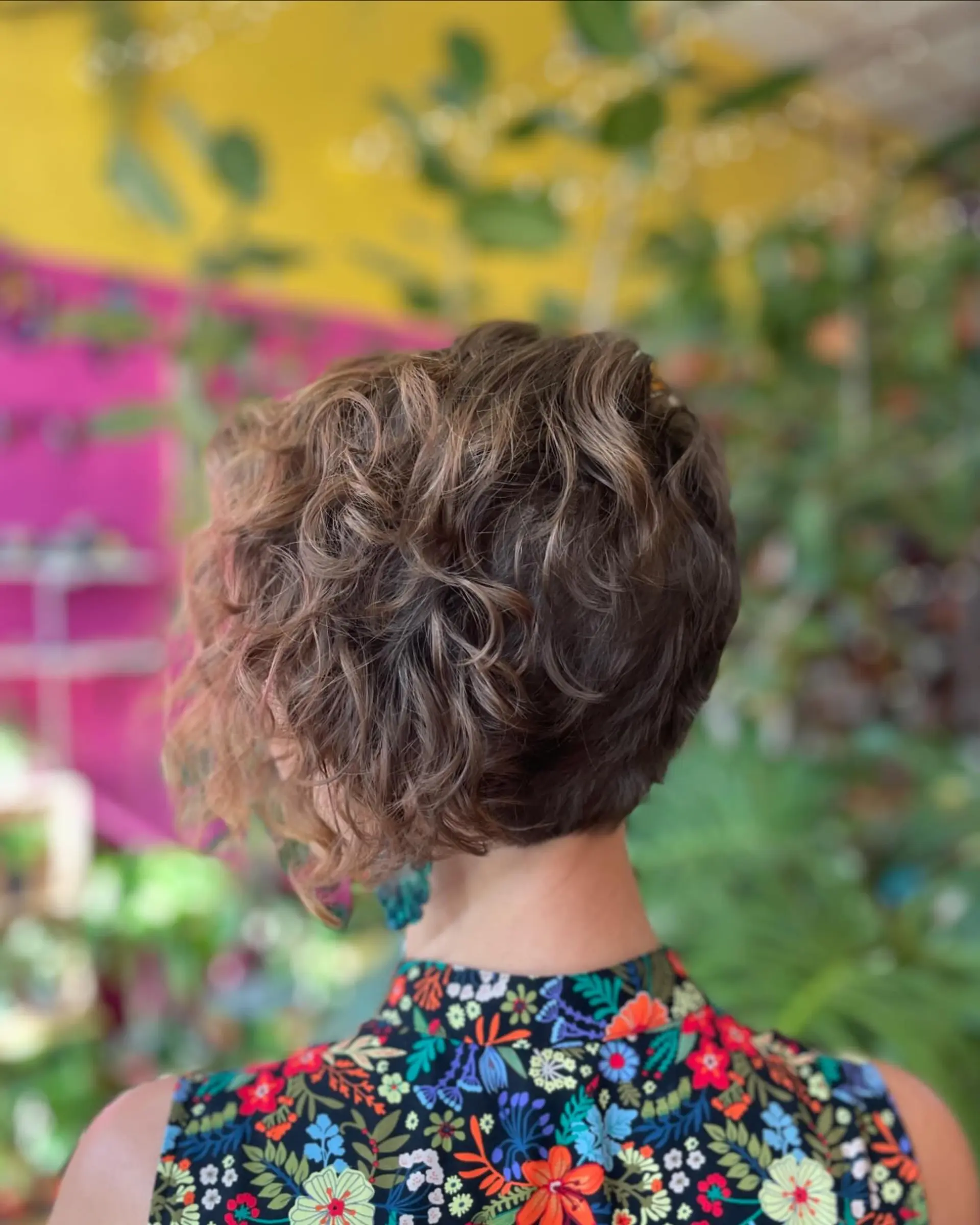 A textured, asymmetrical short cut showcasing natural curls with a tapered nape and longer layers in the front. 1