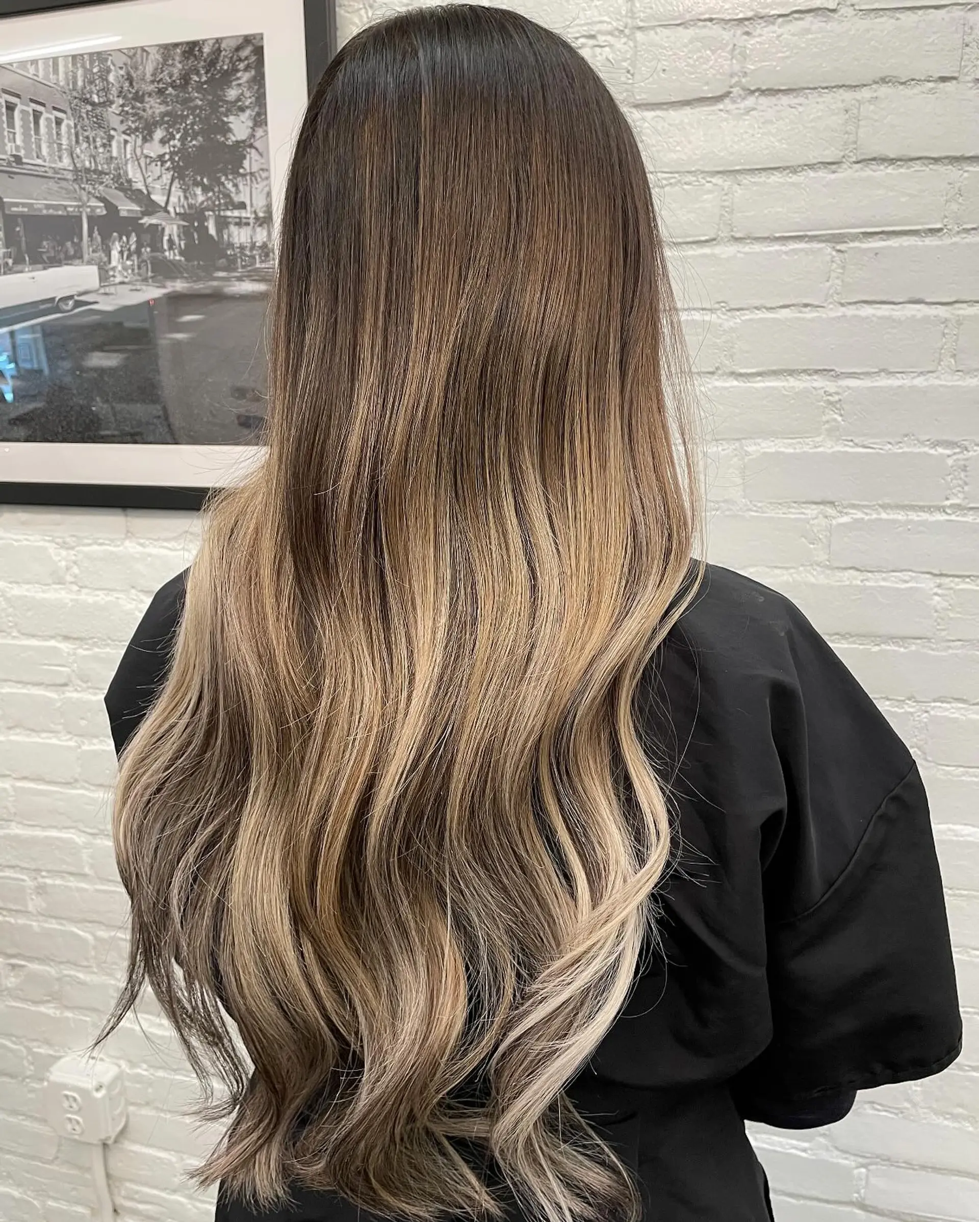 Long hair featuring a deep brunette base blending seamlessly into dimensional blonde tones, styled with gentle waves. 1