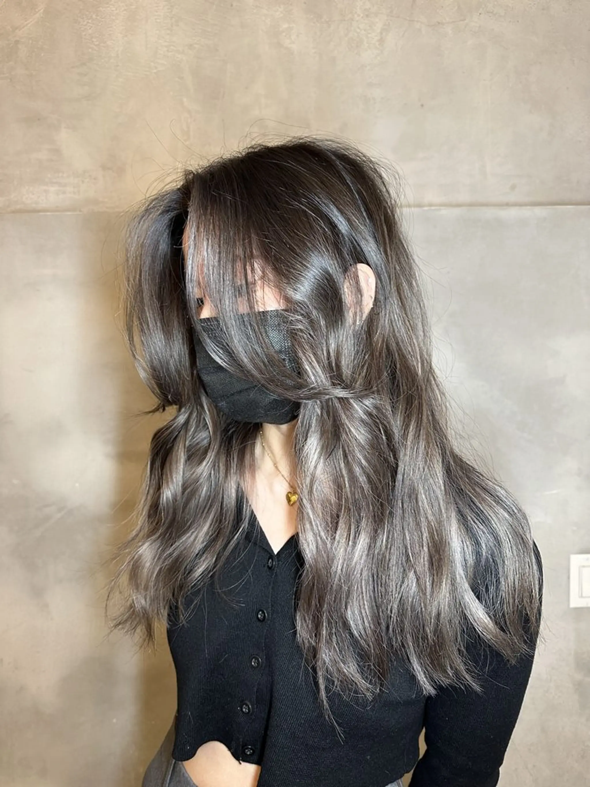 A stunning long, wavy hairstyle featuring a blend of silver and ash gray hues with a color gradient. The hair is styled in voluminous waves with face-framing layers, creating an ethereal, flowing look.
