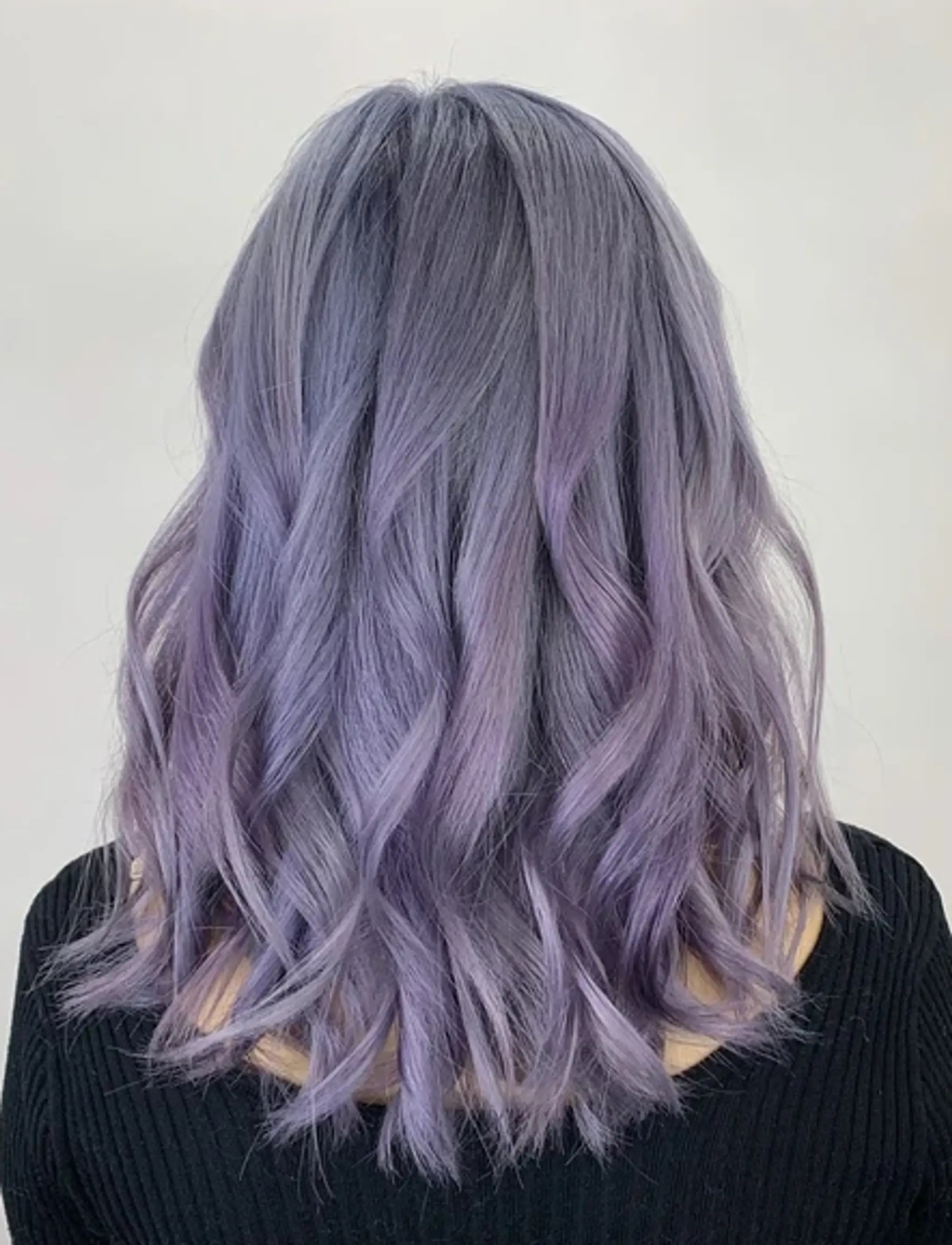 Medium-length, wavy hairstyle with soft waves and a lavender to purple ombre, featuring layered cuts for volume and texture.