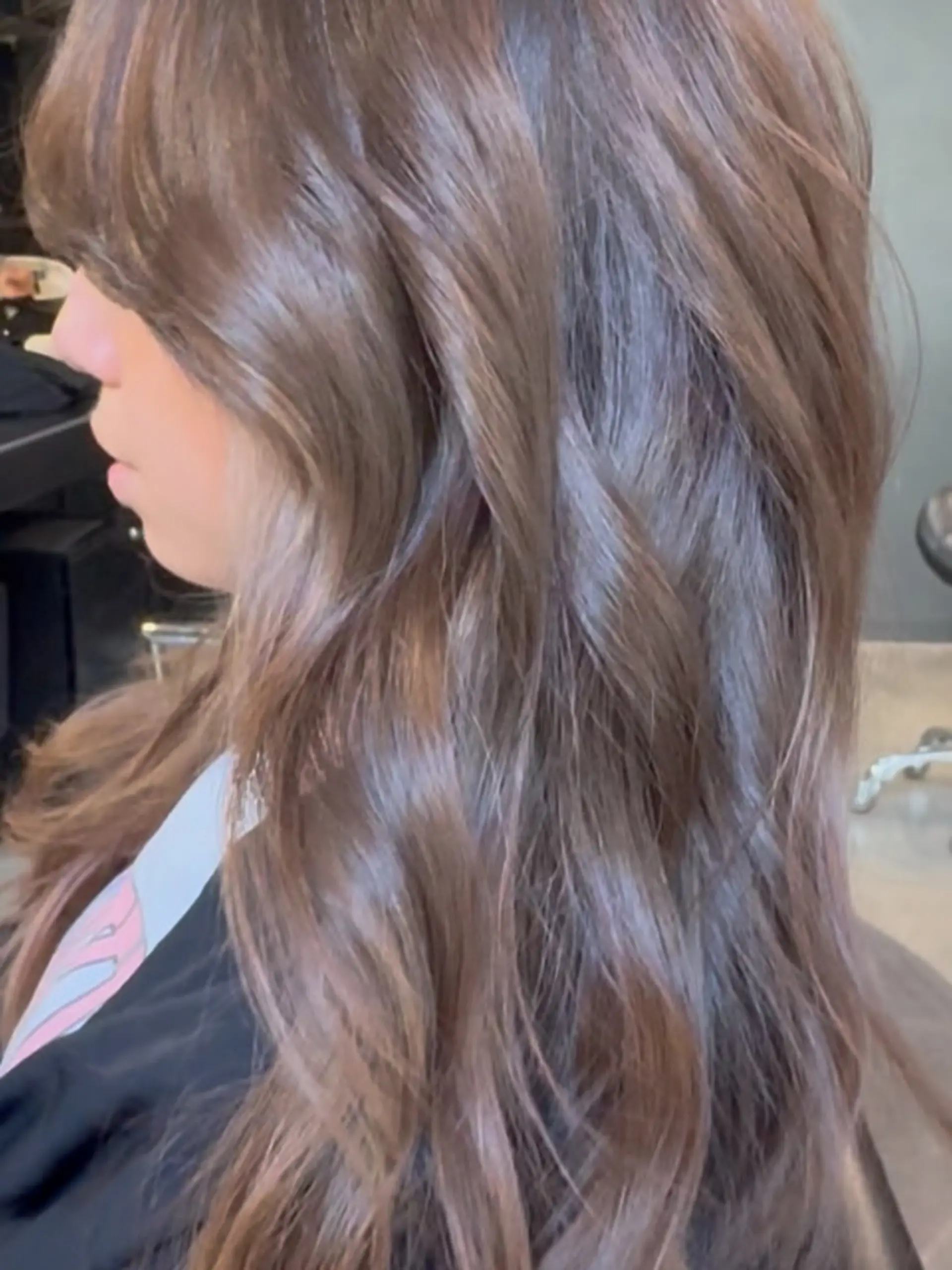 A long brunette layered haircut styled with loose, effortless waves and soft face-framing bangs. 1