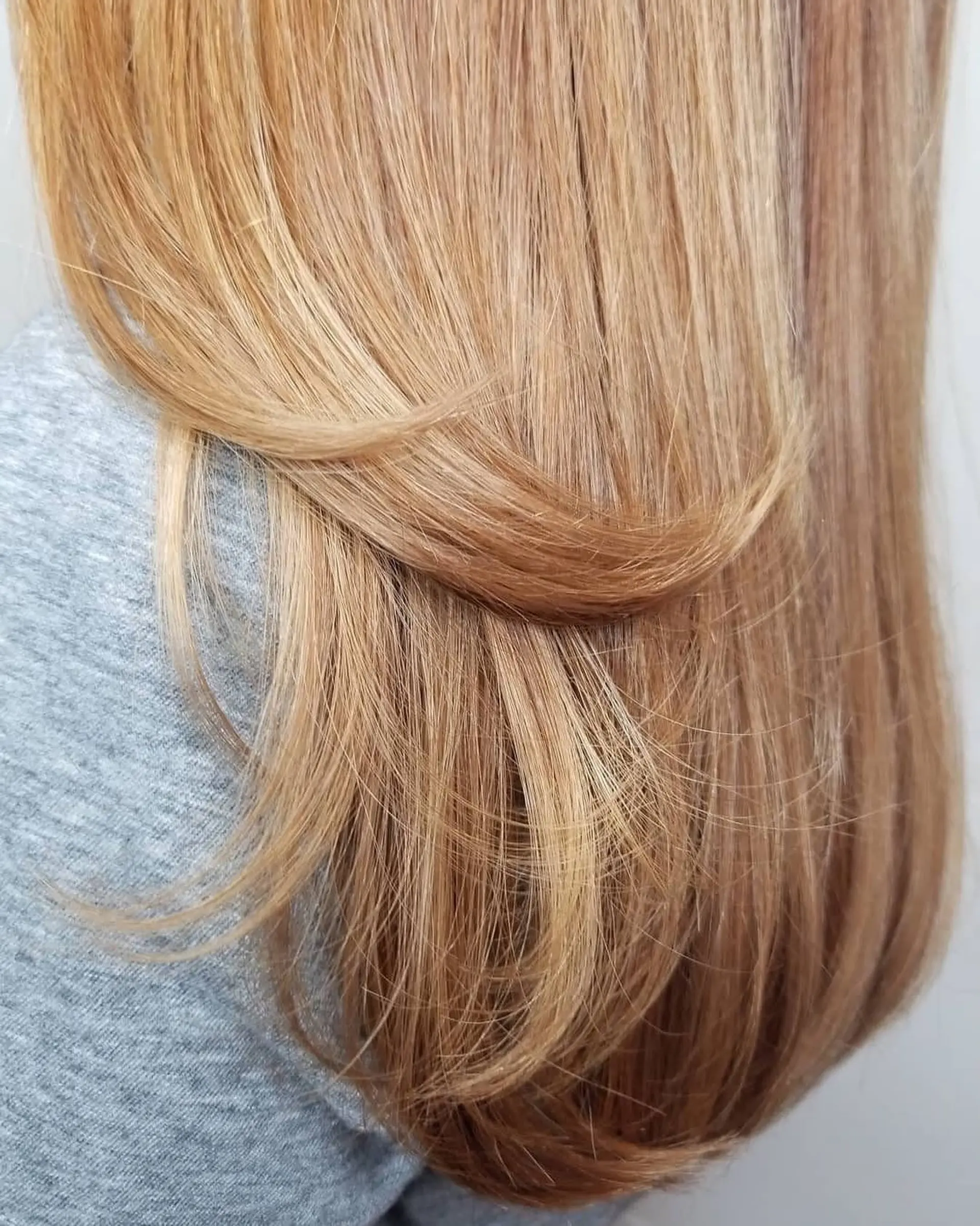 A long, silky warm blonde blowout styled smooth with layered dimension and a soft curved finish. 1