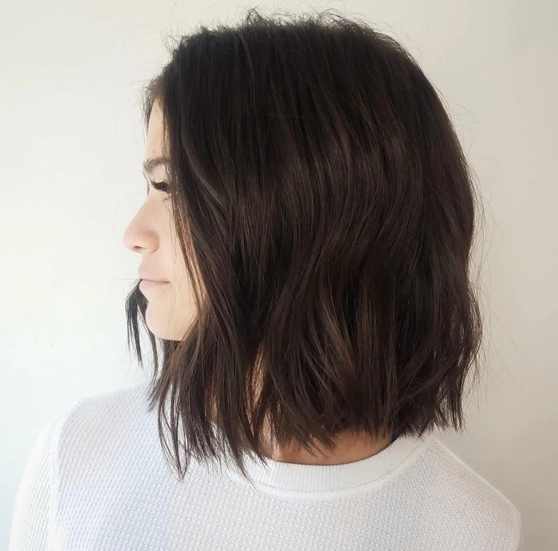 A blunt, textured chin-to-collar-length bob styled with soft, lived-in waves in a rich dark brunette tone. 1