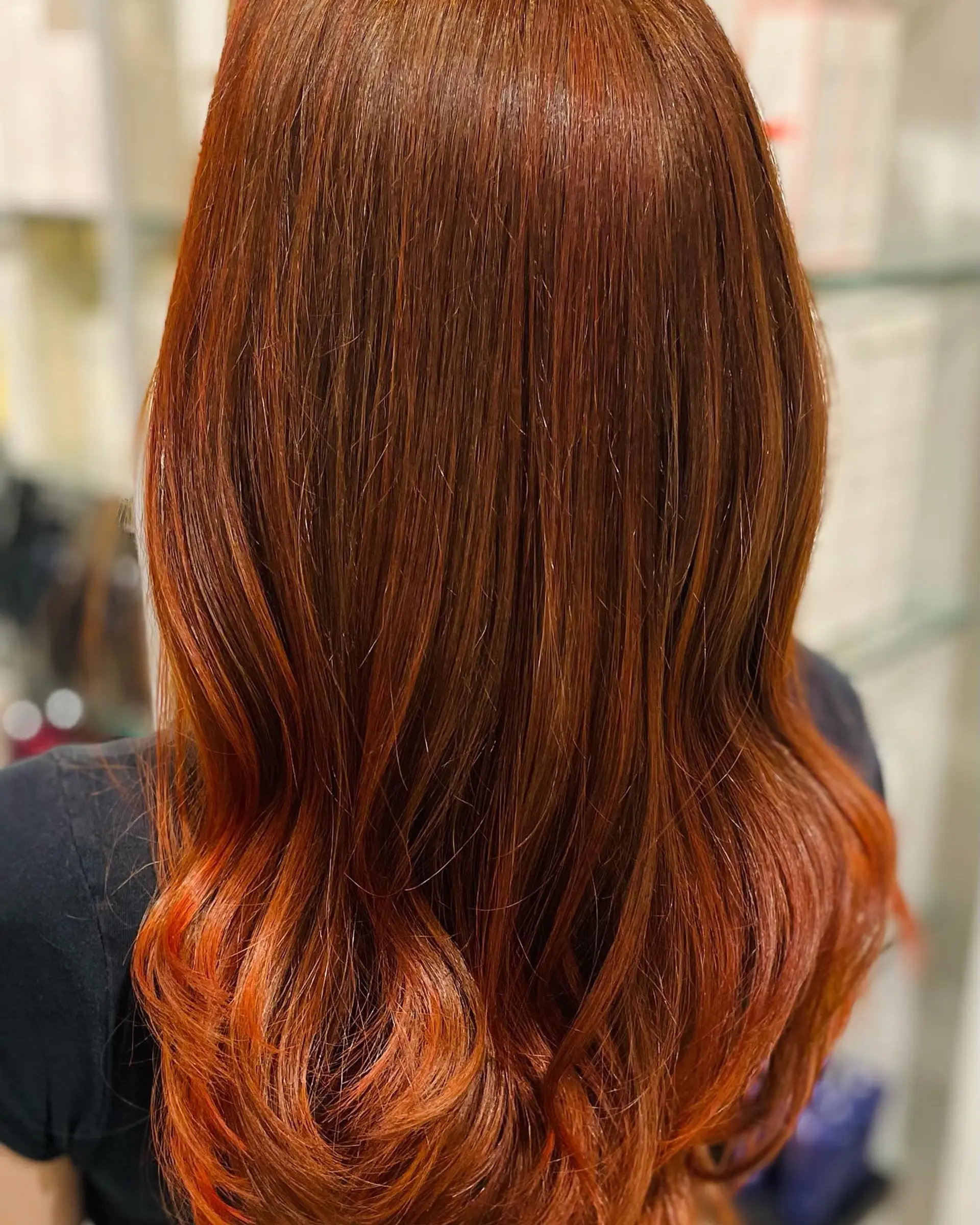 Long warm auburn and copper-red hair styled straight through the lengths with soft curling at the ends. 1