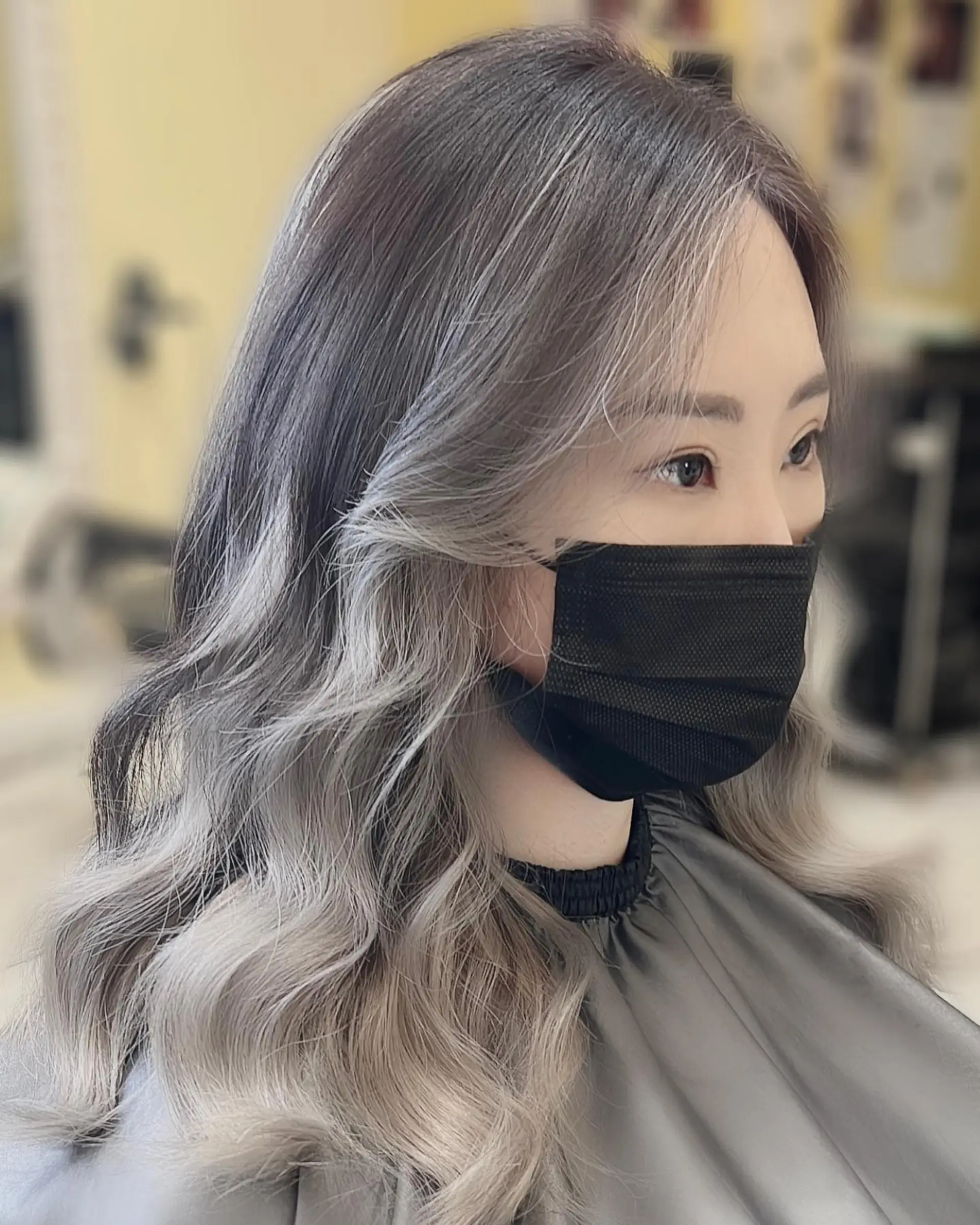A wavy medium-length hairstyle featuring a shadow root, ash blonde balayage, and a prominent money piece. 2