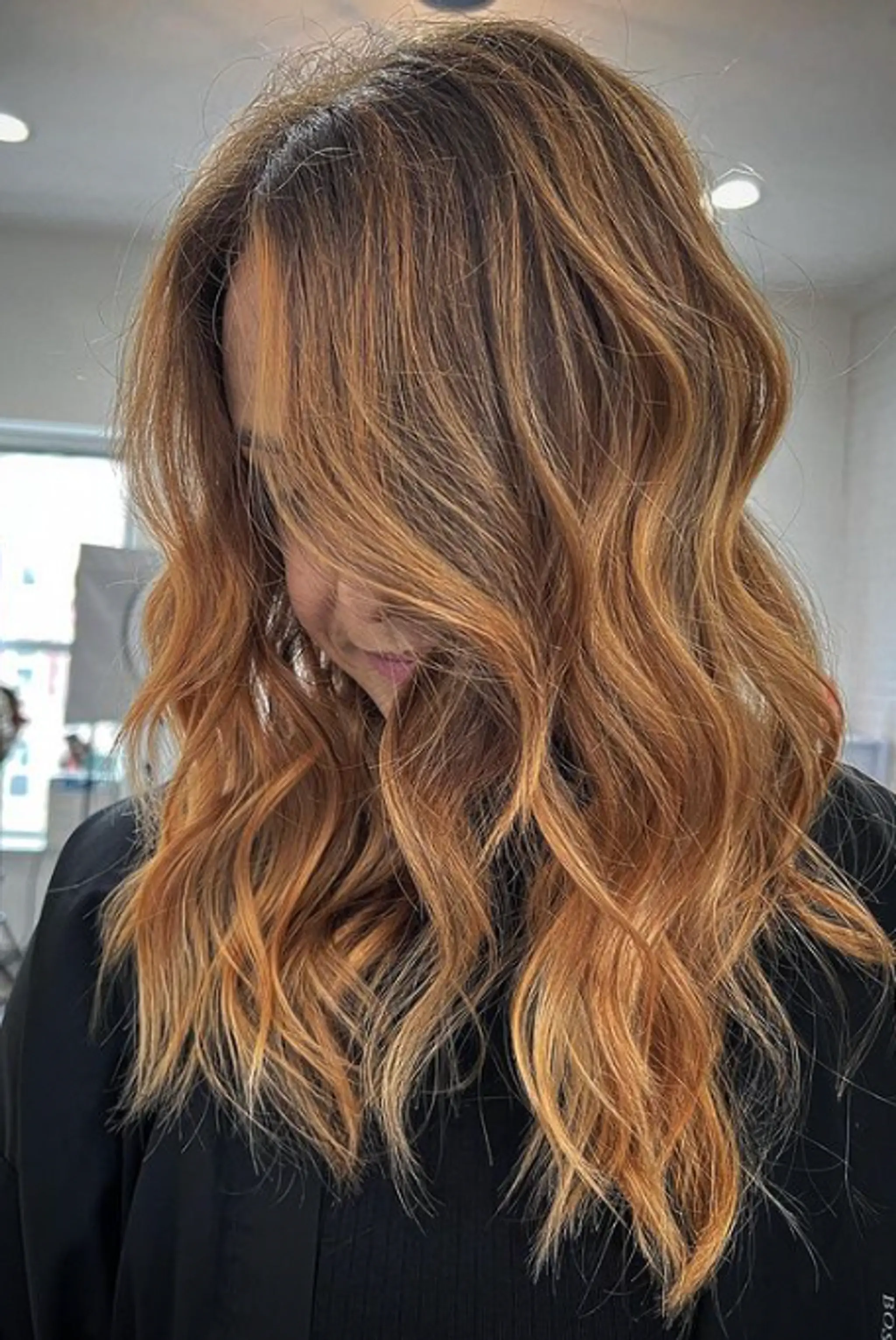 Long, honey blonde to dirty blonde hair with soft, natural waves. The style includes layered cuts that frame the face, with a sun-kissed highlight adding subtle volume and movement.