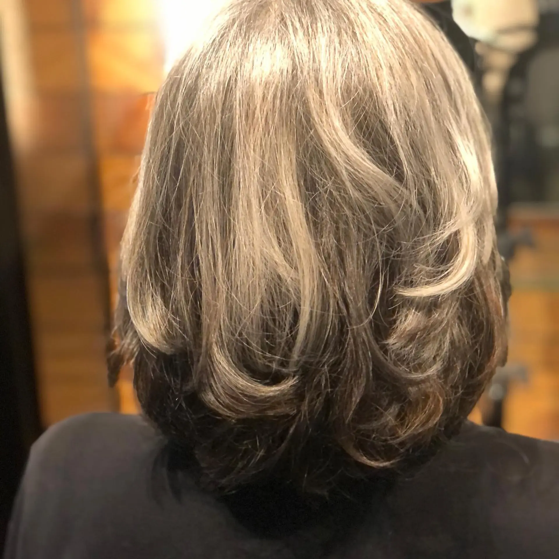 Medium-length layered cut styled with soft curled ends, showcasing grey and silver dimension over a dark brunette base. 1