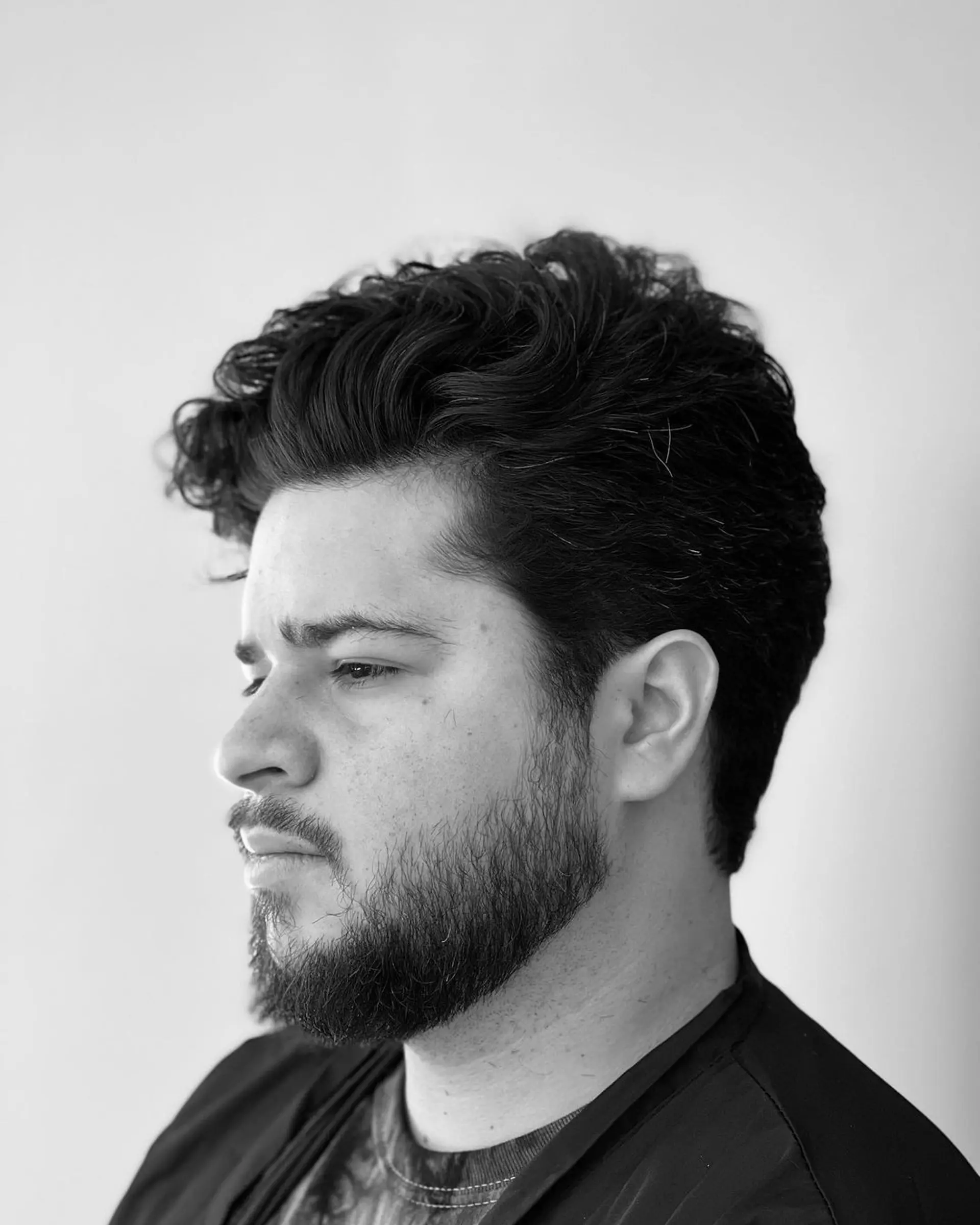 Medium-length, wavy hairstyle with natural volume and texture. The sides are slightly shorter, and the look is complemented by a well-groomed beard.

 2