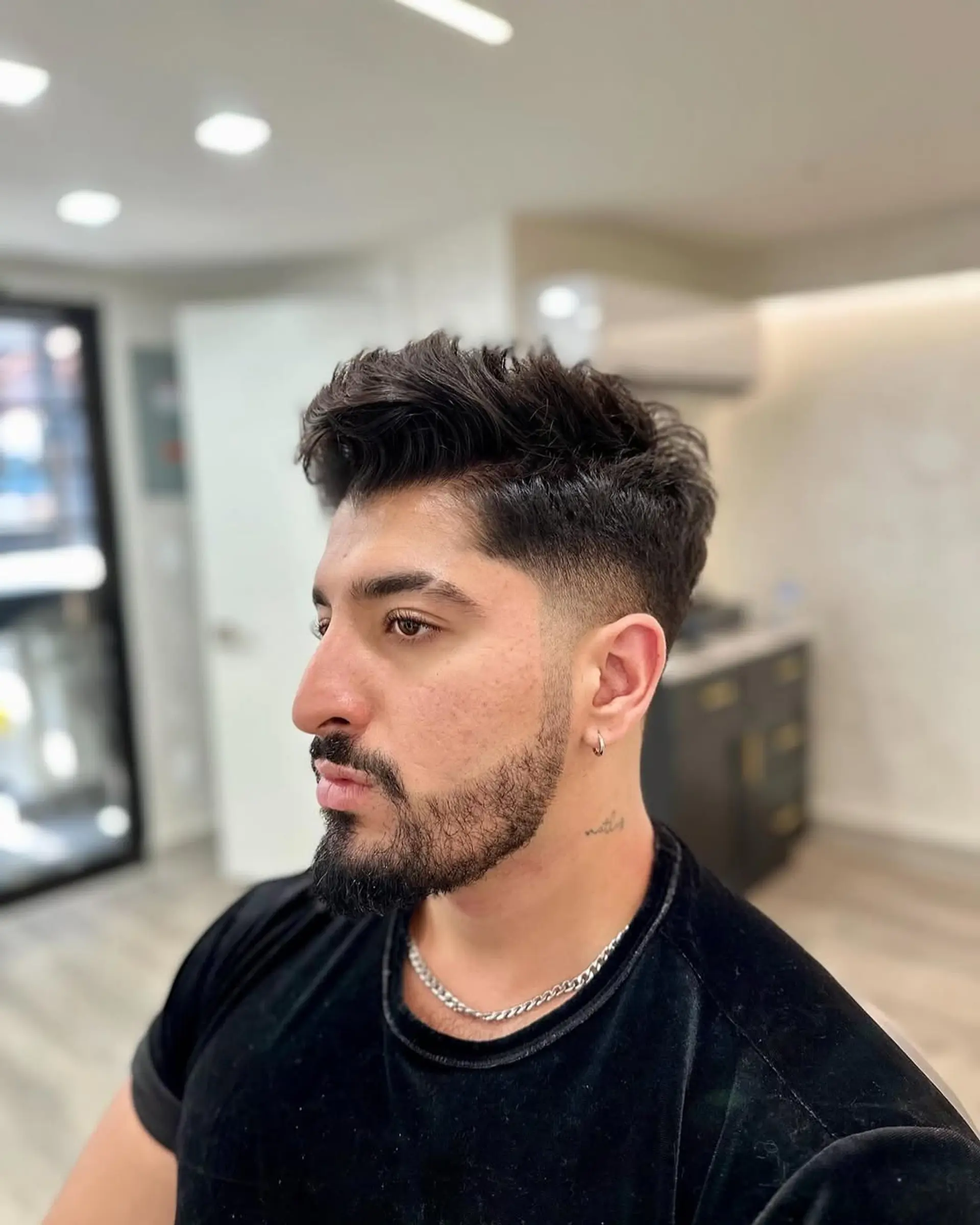 A trendy men's textured crop fade haircut with longer, voluminous wavy hair styled on top, complemented by clean faded sides and a well-defined beard. 1