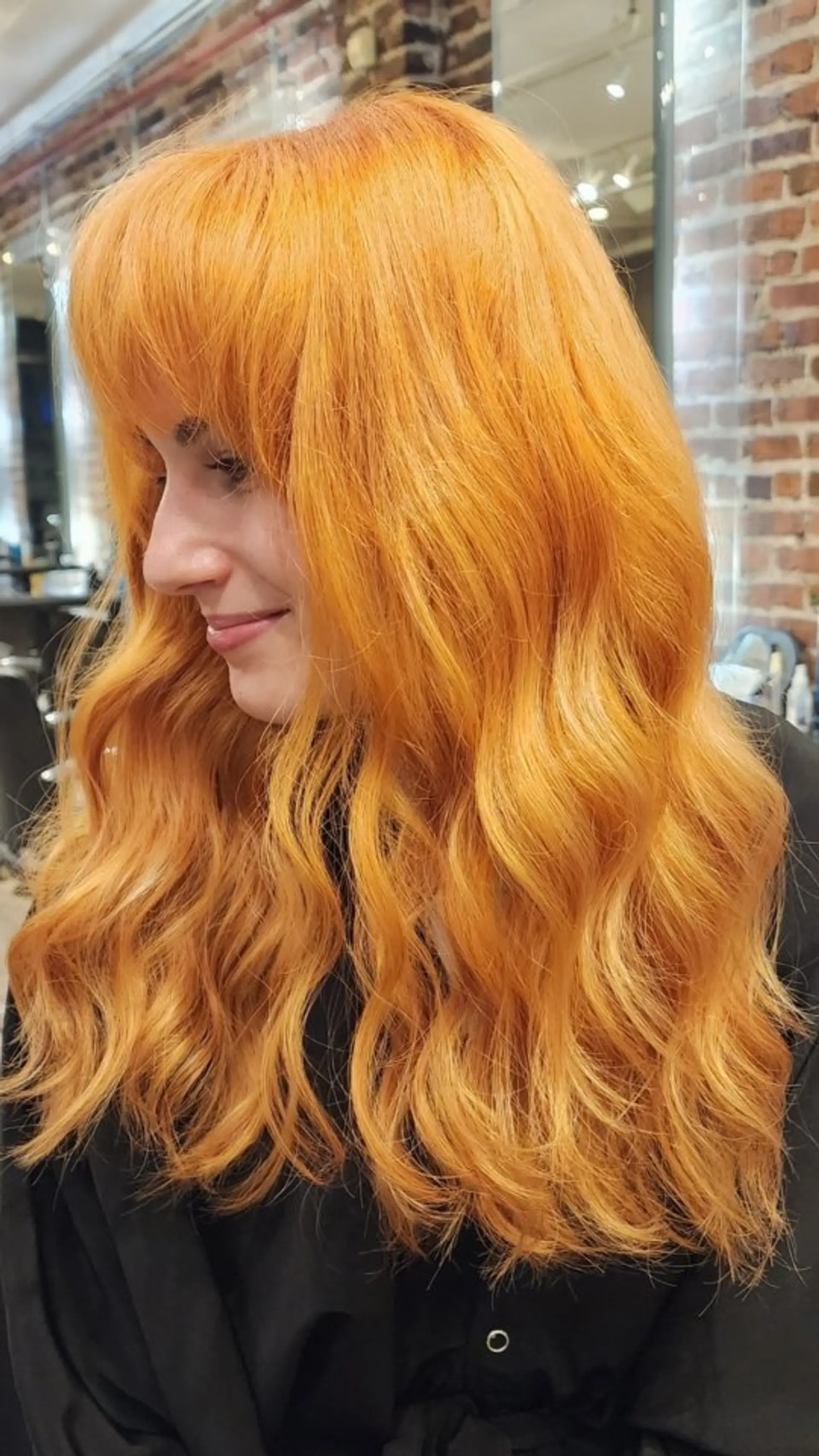 Vibrant, all-over bright copper hair styled in soft, loose waves with full front bangs. 1