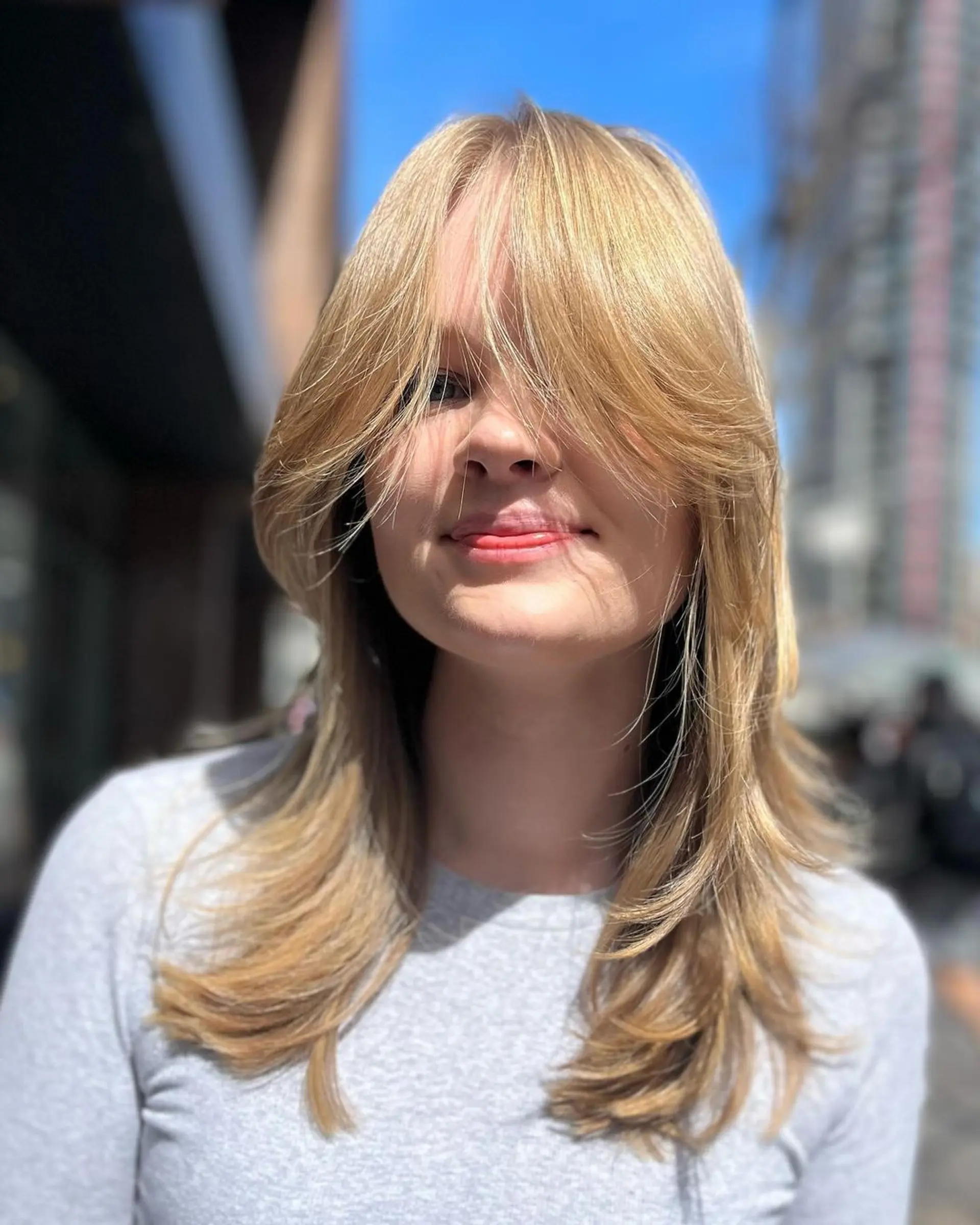 Medium-length, straight, blonde hair with layered, feathered ends and side bangs that blend into the style. 1