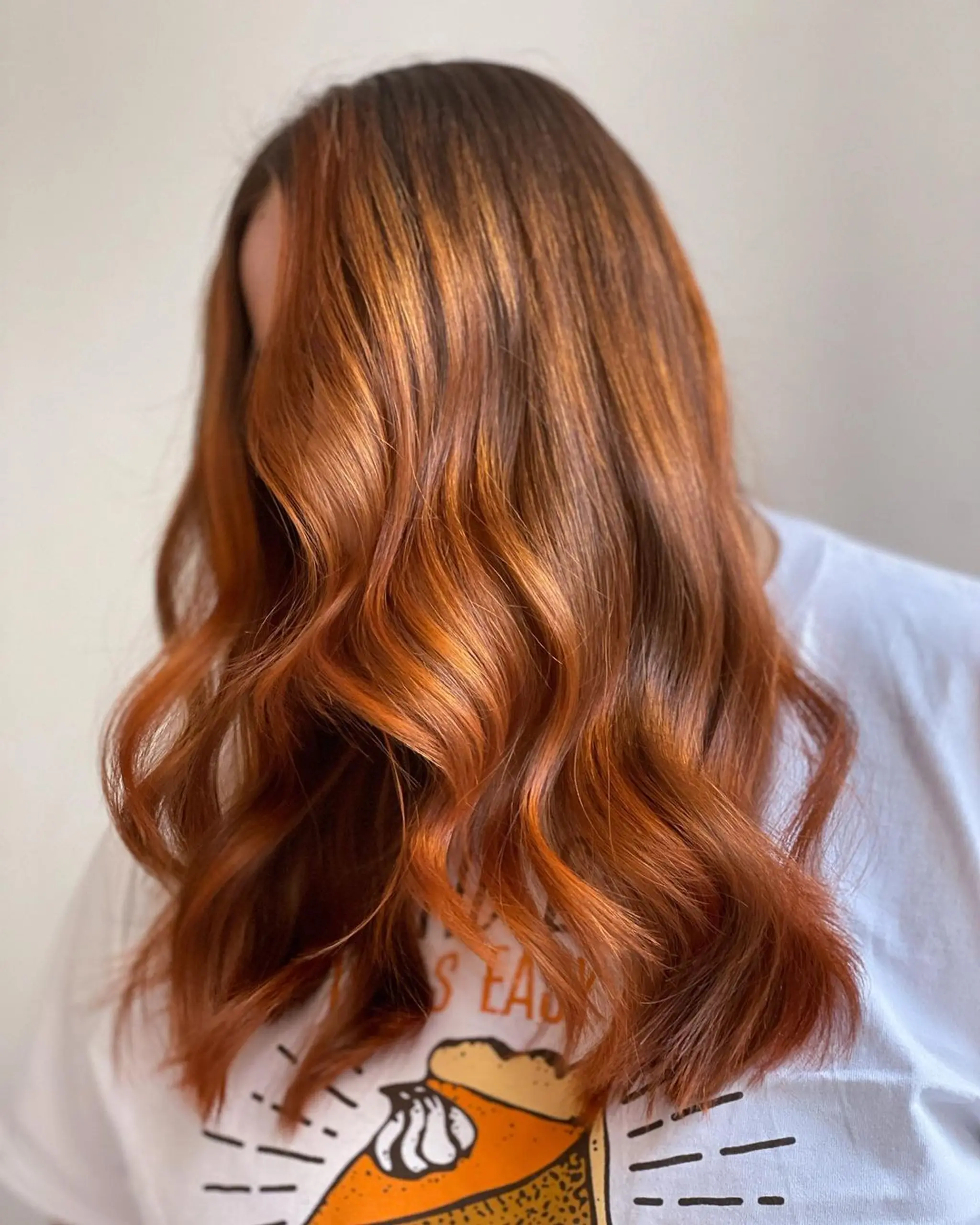 Medium length wavy hair with copper color and auburn highlights, styled in loose, voluminous waves.