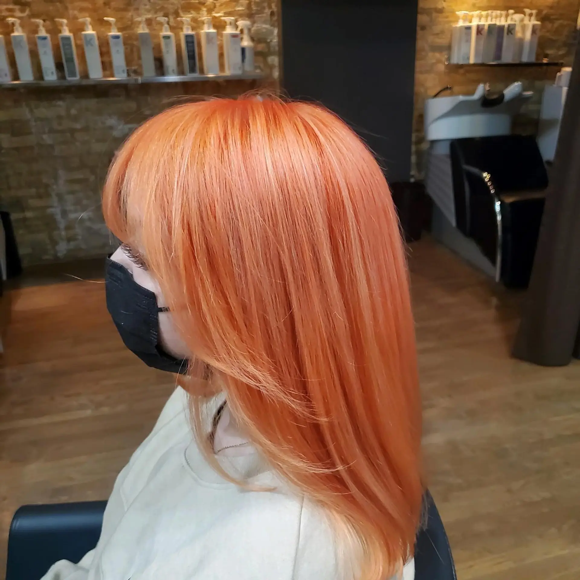 A sleek medium-length straight hairstyle featuring blunt bangs and an all-over vibrant peach-orange shade. 1