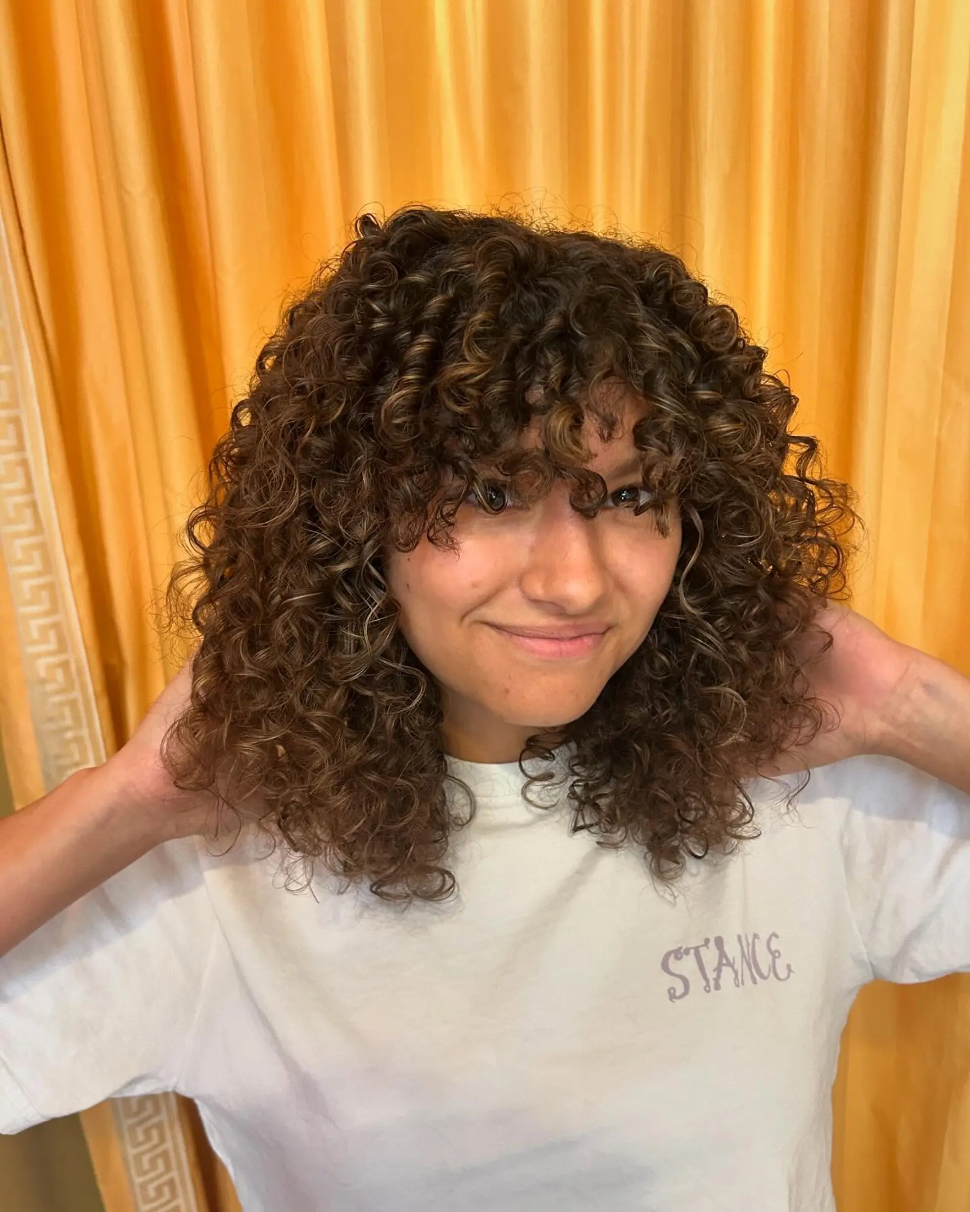 Medium-length curly shag featuring defined ringlets, rounded layering, face-framing curly bangs, and warm dimensional highlights. 1