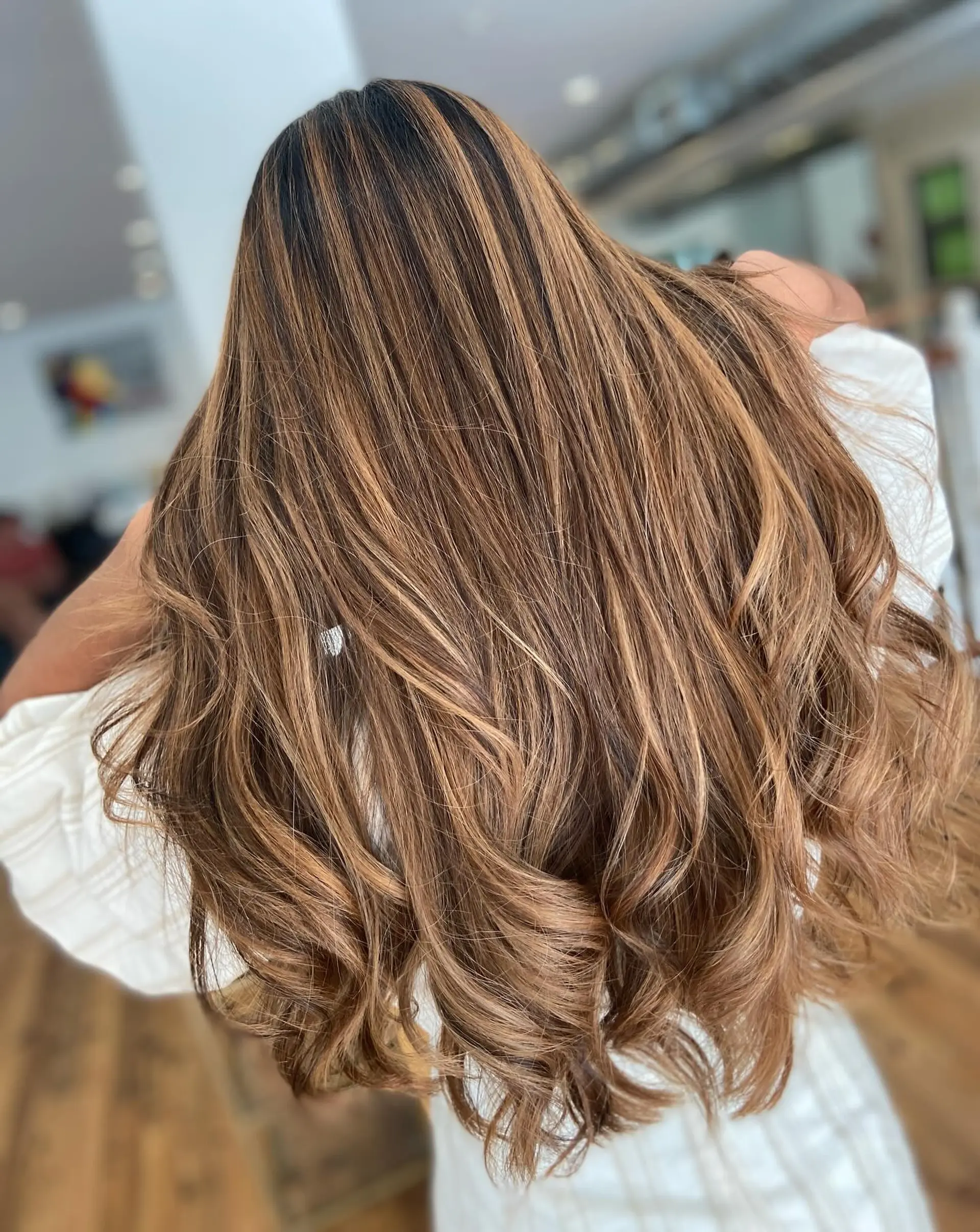 A very long, layered hairstyle featuring a caramel swirl balayage with soft waves and blended color. 1