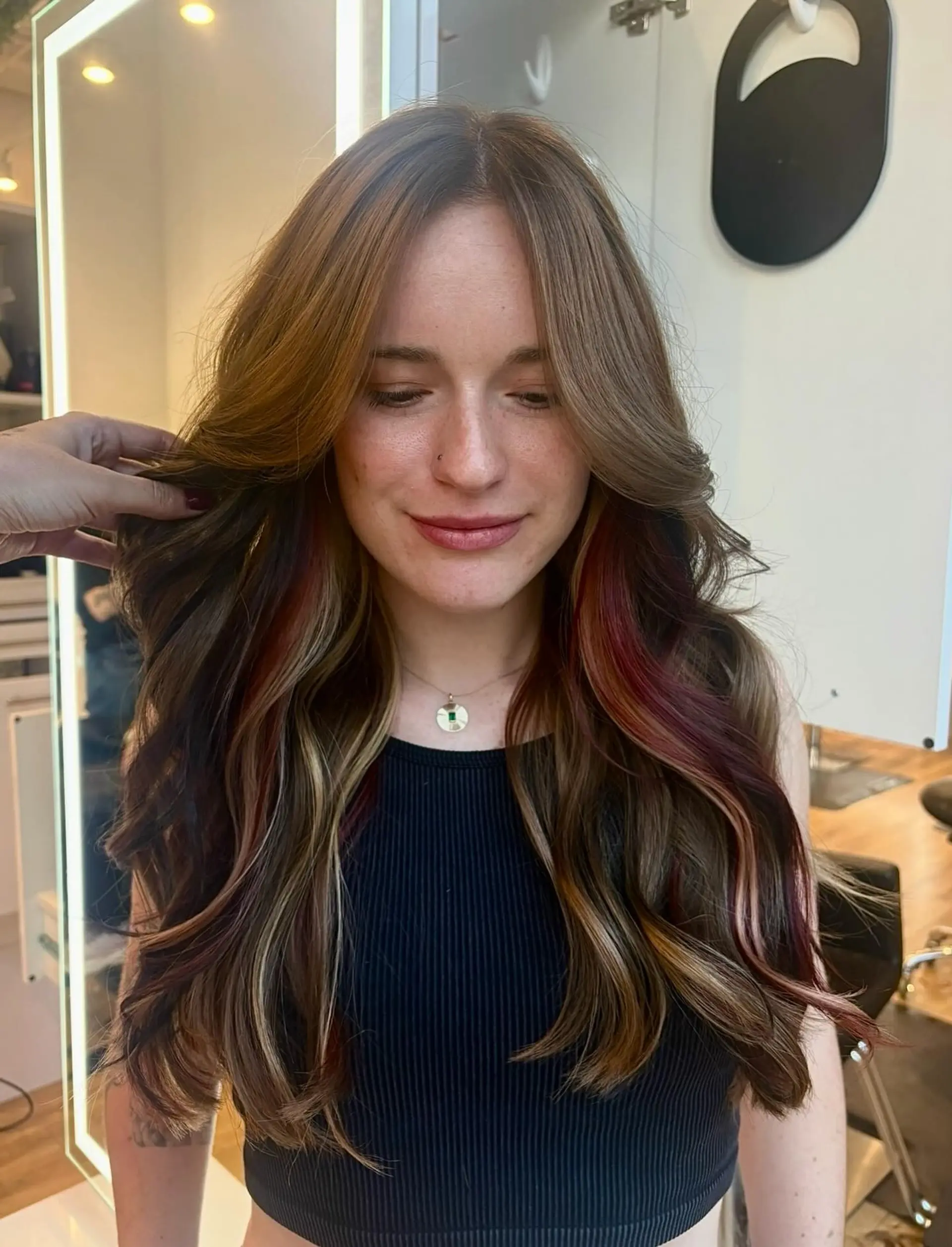 Long layered brown hair with soft waves, curtain bangs, and peekaboo red and blonde highlights. 1