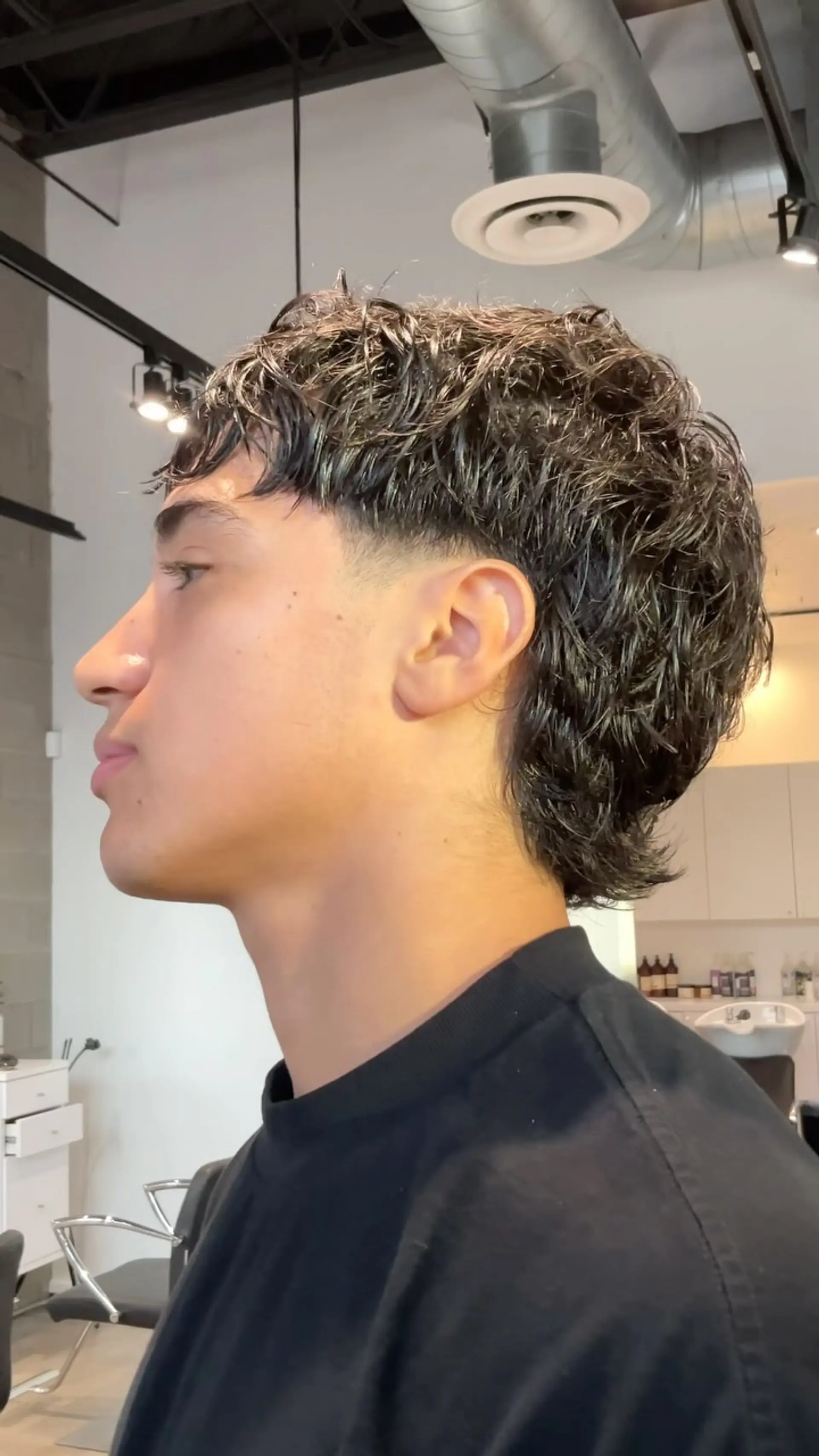 A modern curly mullet featuring a clean temple taper fade, textured fringe, and layered wavy length along the back. 1