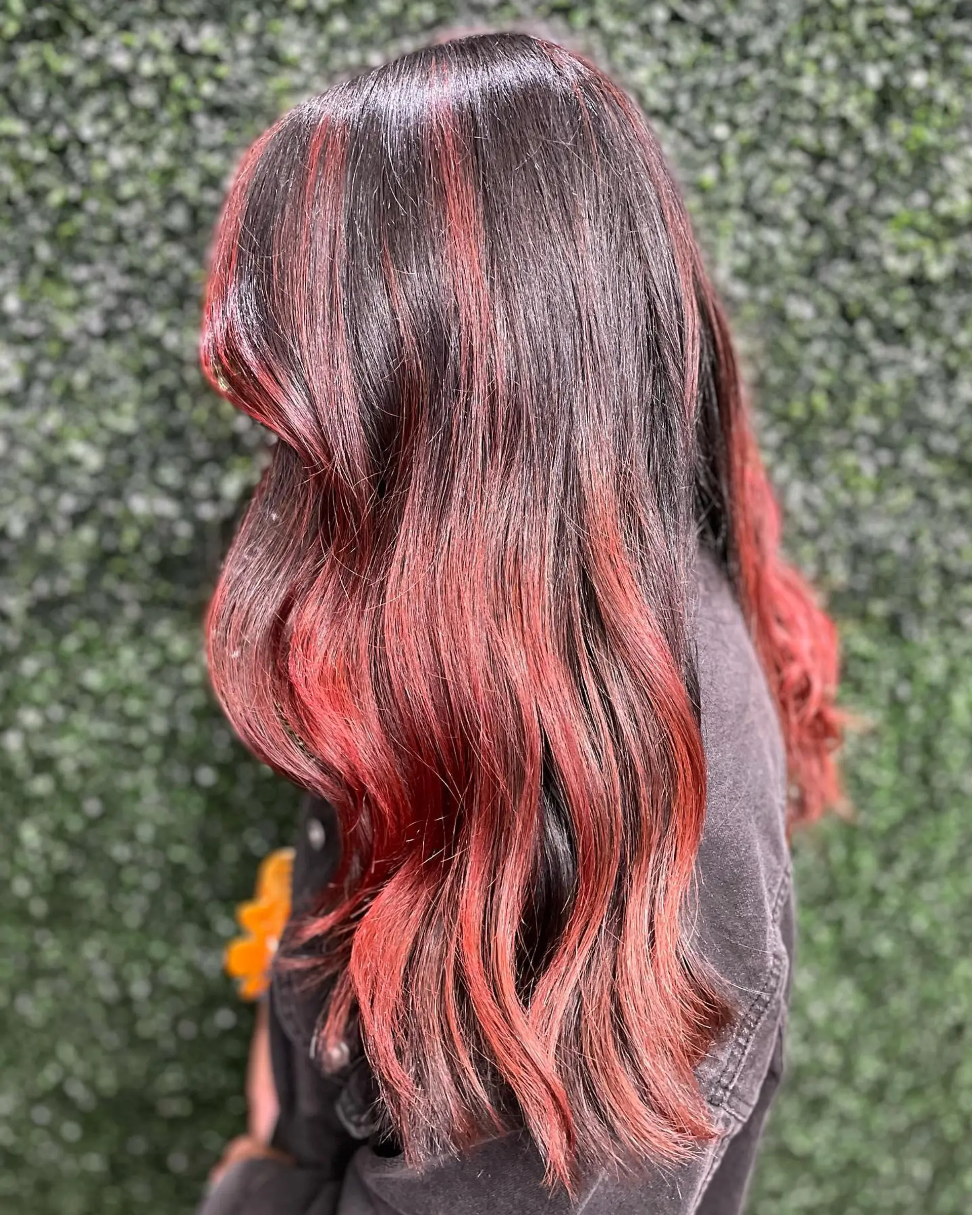 Long dark hair accented with rich crimson red balayage highlights and styled in soft waves. 1
