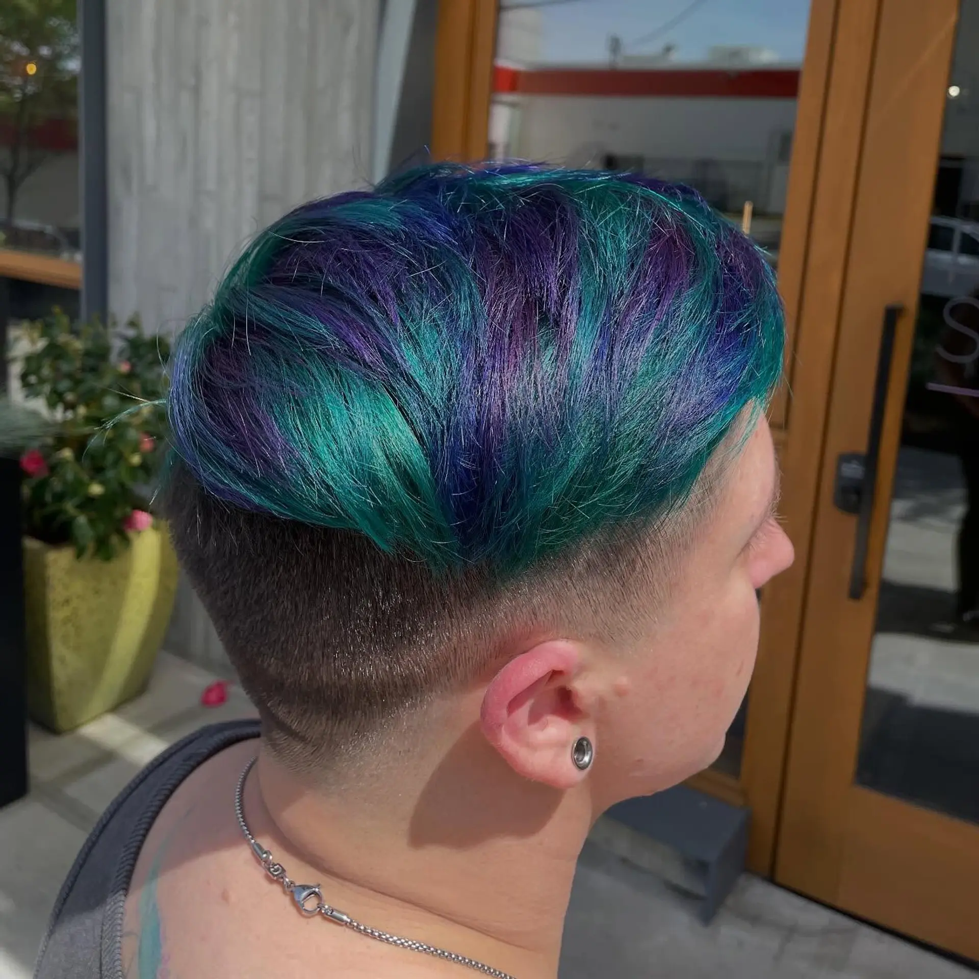 A short pixie cut with a clean undercut fade on the sides and back, featuring textured top layers colored in vibrant peacock teal, royal blue, and deep purple. 1