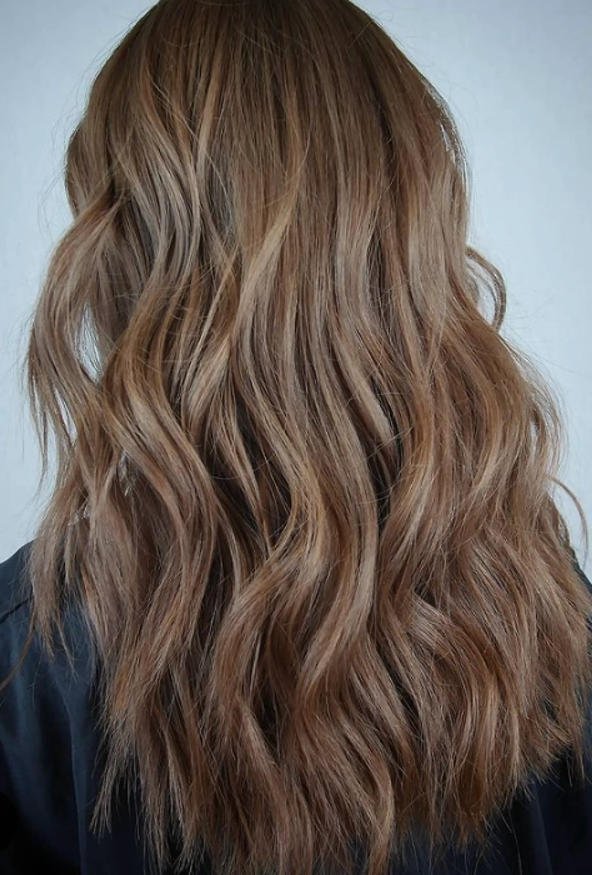 Medium-length, light brown wavy hair with caramel highlights. Features natural waves and textured layers for a beachy, sun-kissed look.