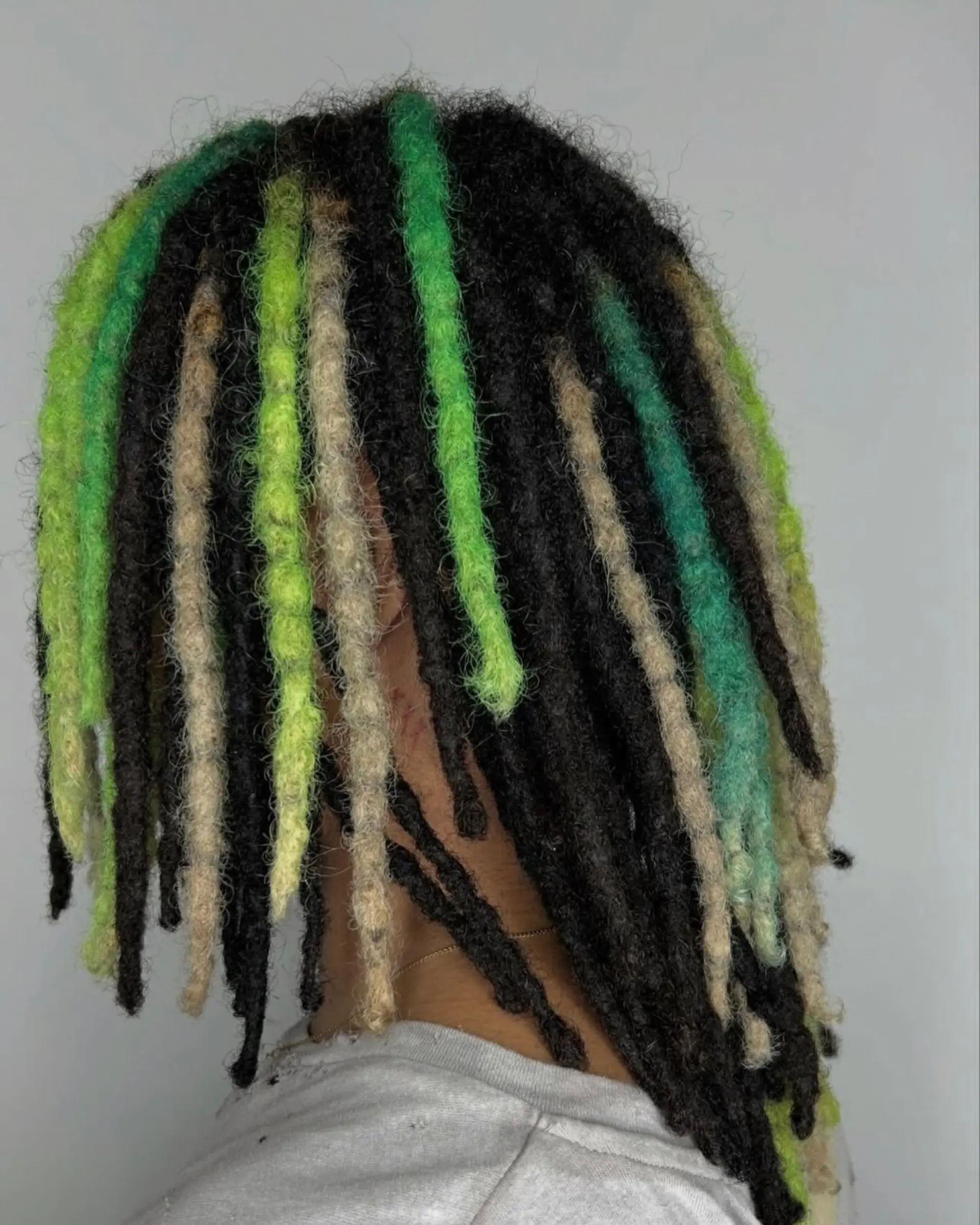 Medium-length dreadlocks featuring high-contrast vivid neon green, teal, and ash-blonde highlighted locs mixed throughout a dark base. 1