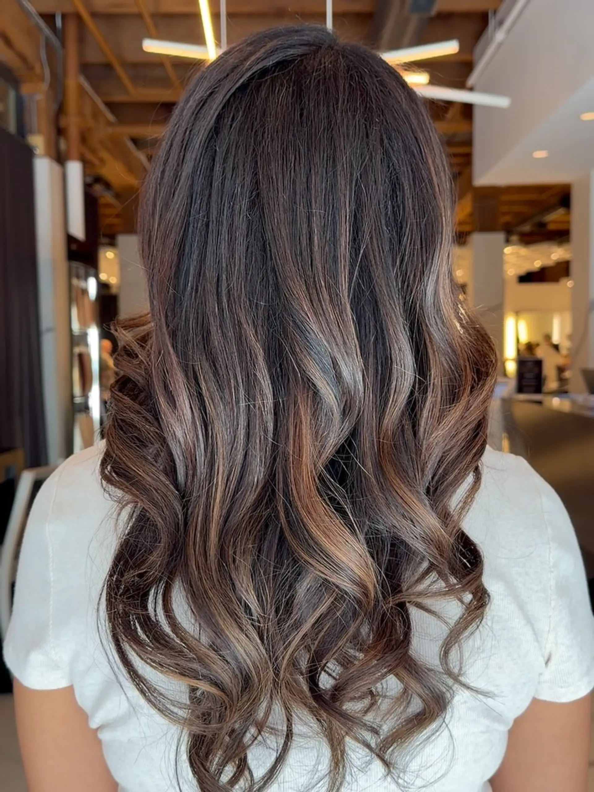Long brunette hair with soft dimensional balayage highlights styled in glossy, loose waves. 1