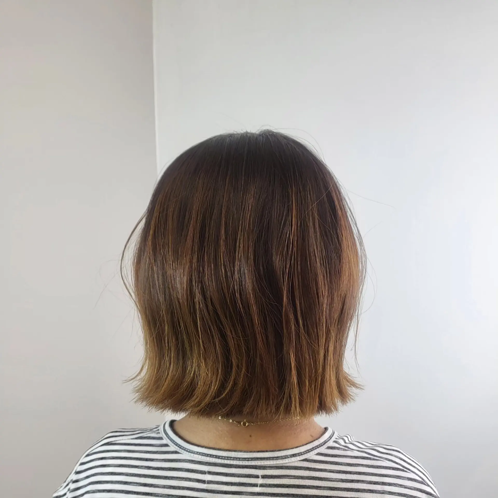 A blunt neck-length bob styled straight with subtly flipped-out, textured ends and warm caramel undertones. 1