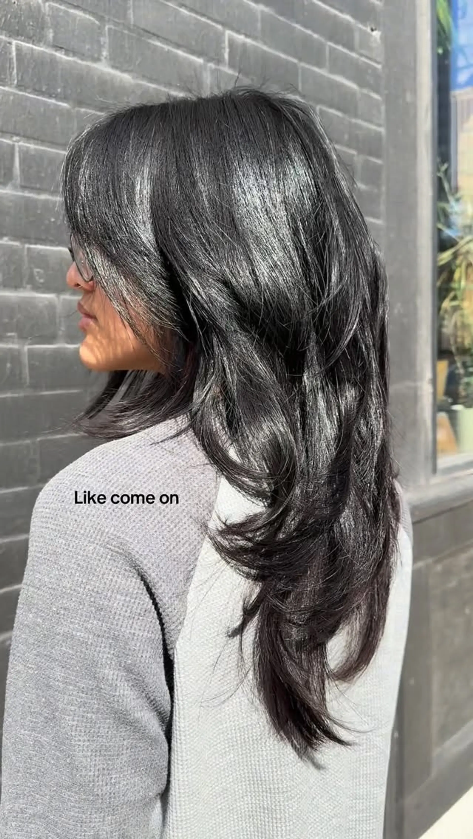 A glossy, long dark haircut featuring cascading textured layers and softly swept face-framing bangs. 1