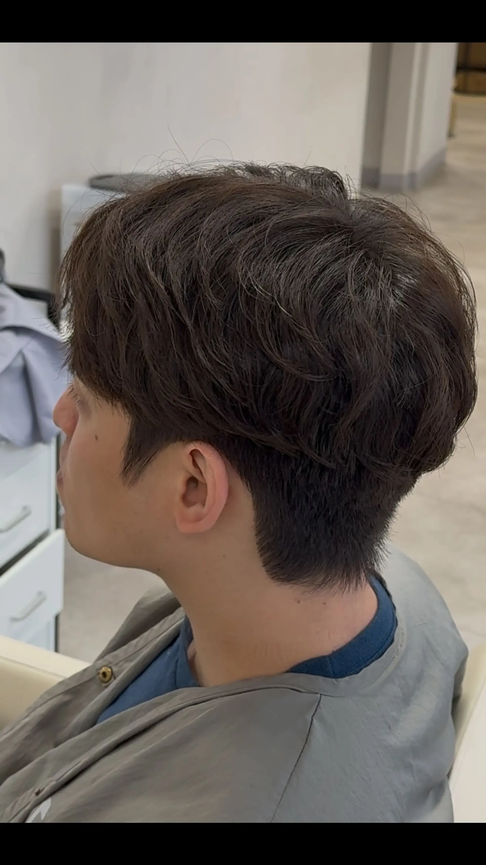 A short men's two-block haircut styled with natural, voluminous waves created through a perm, paired with neatly tapered sides and back. 1