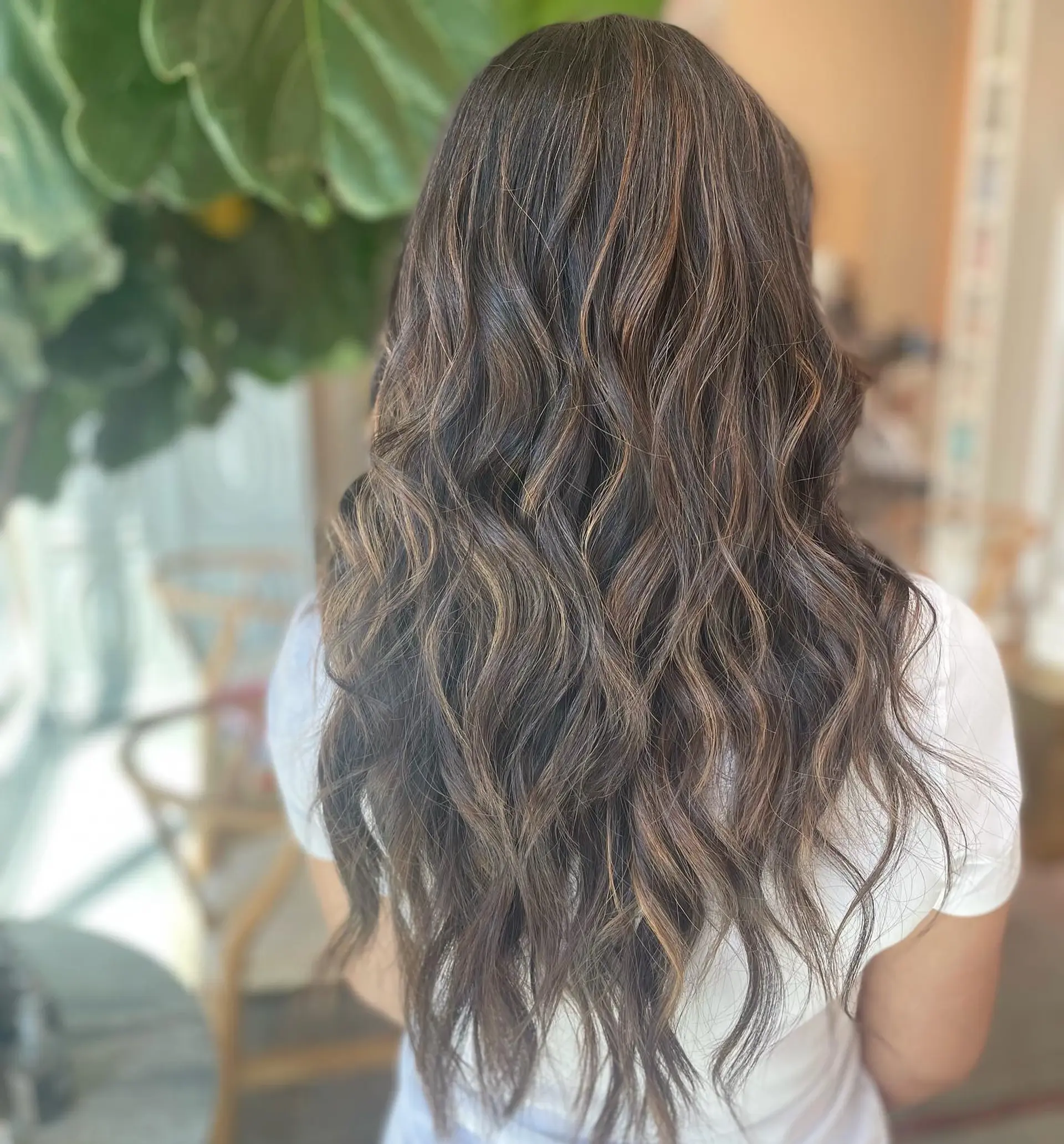 Long dimensional brunette hair styled in loose, textured waves with subtle caramel balayage highlights. 1