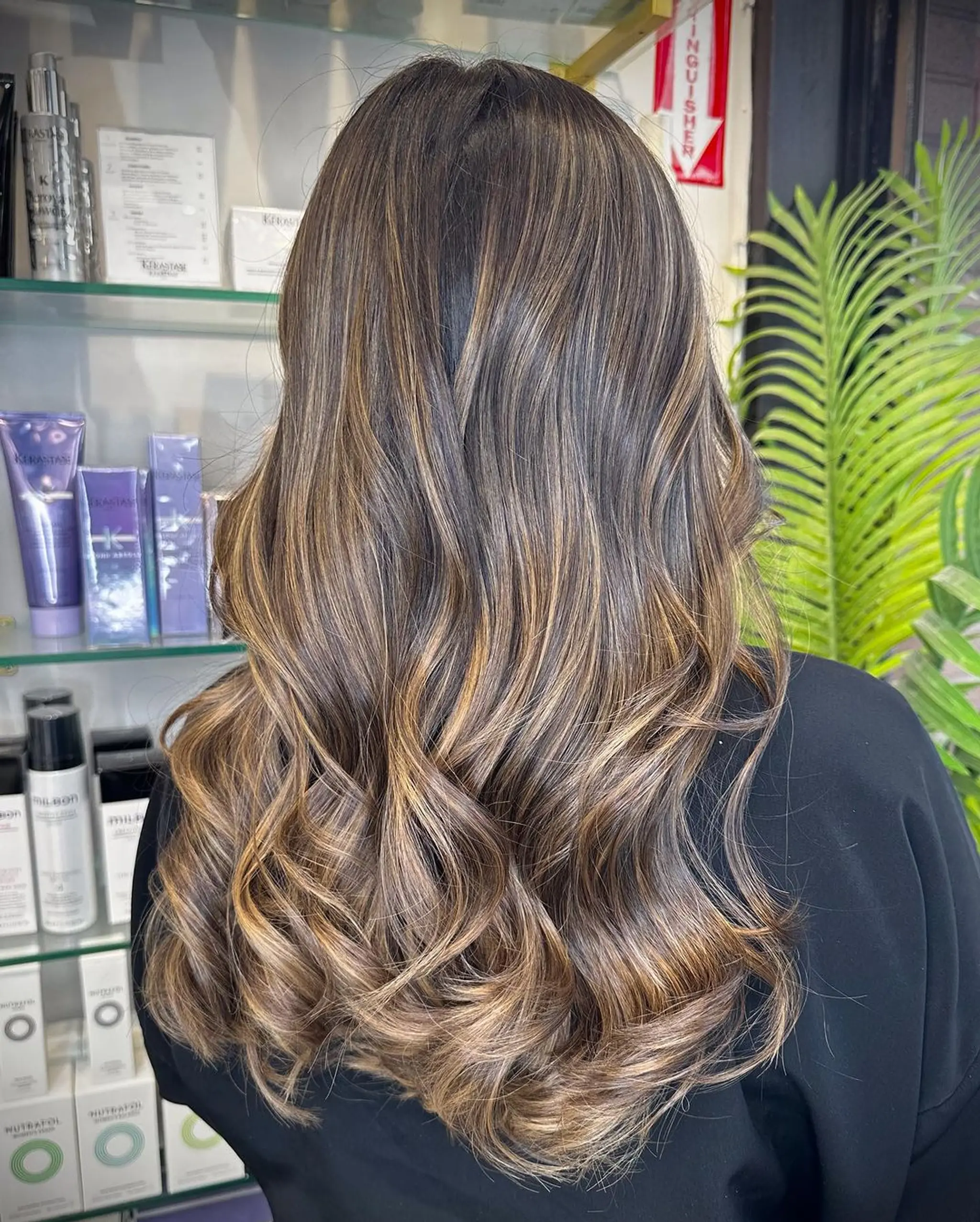 Long, wavy hair with a rich brown base and blonde highlights, featuring natural soft curls and a sun-kissed effect.