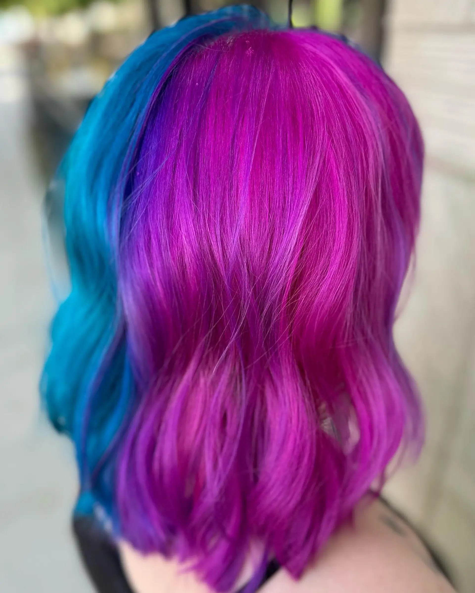A bold split-dye look featuring electric cyan blue on one side and vibrant magenta fading into violet on the other, styled with soft dimensional waves. 1