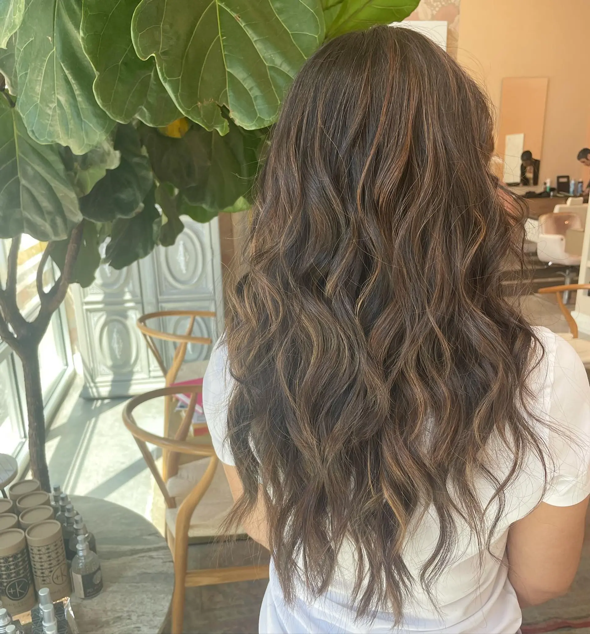 Long dark brunette hair styled in loose, textured waves with subtle caramel and warm brown balayage highlights throughout. 1