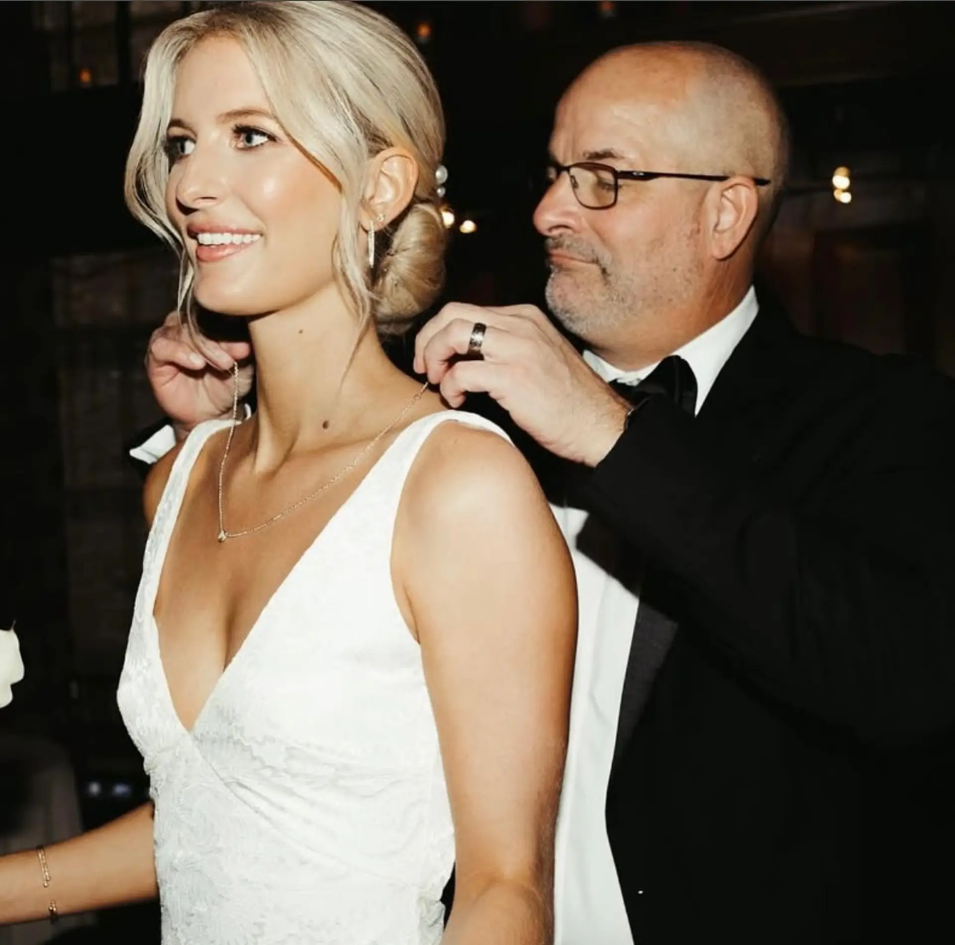 An elegant bridal low bun updo featuring soft, face-framing tendrils parted down the middle. 1