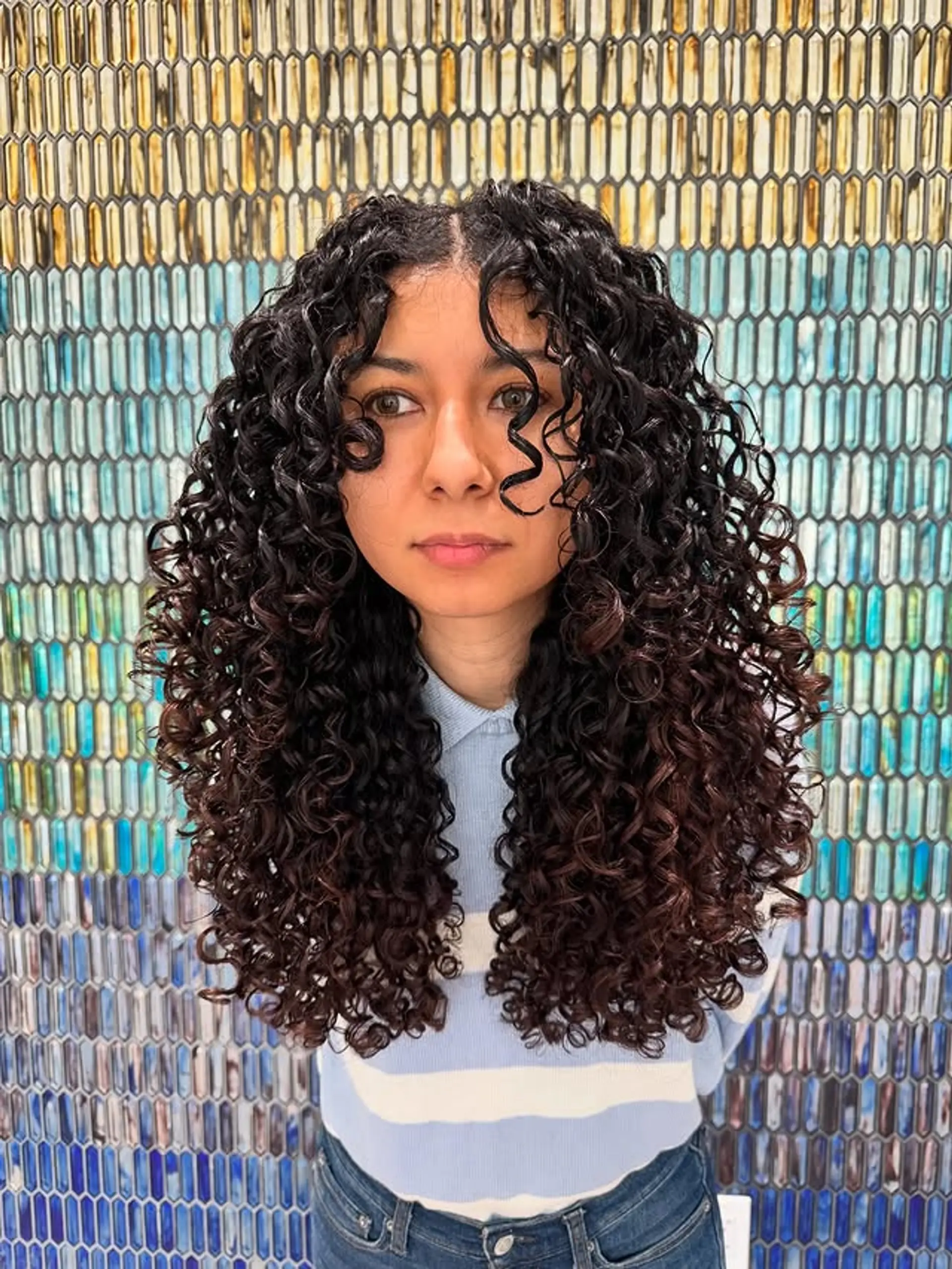 Long, layered curly hairstyle featuring defined ringlets and soft curtain bangs. 1