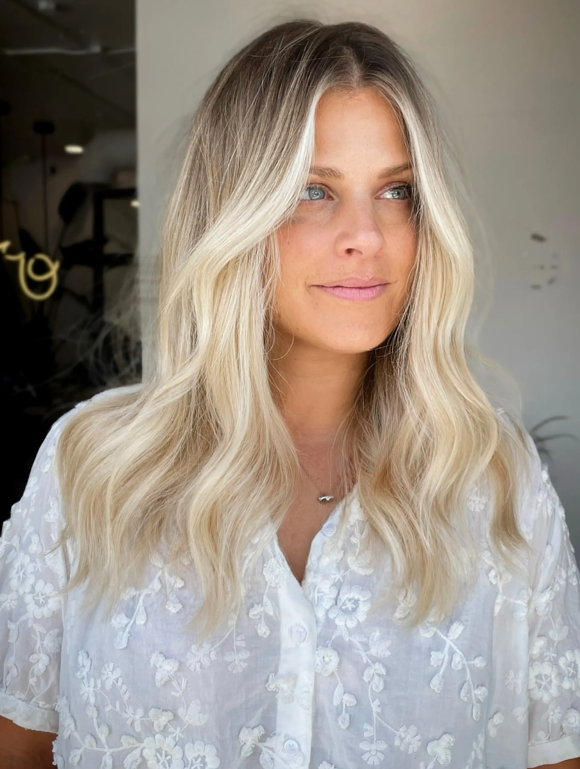 Long bright blonde hair featuring a seamless balayage blend, bright face-framing money pieces, and soft beach waves. 1