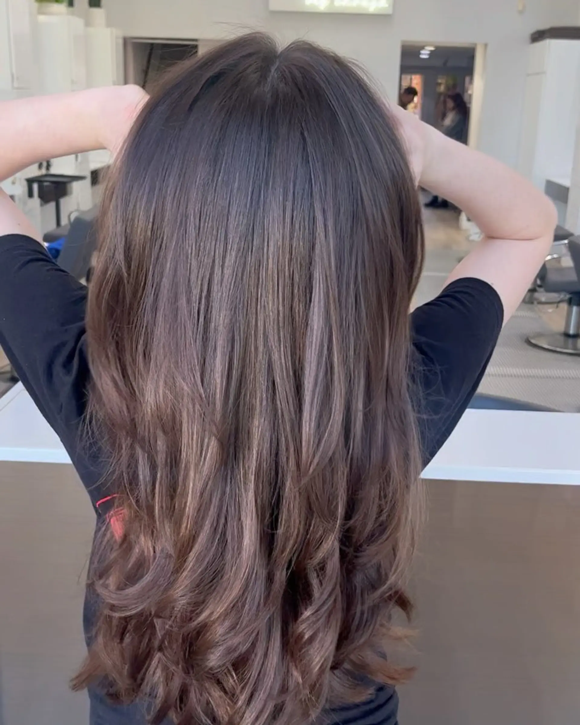 Long cascading brunette hair cut with multi-dimensional layers and styled with a round brush blowout for soft, bouncy ends. 1