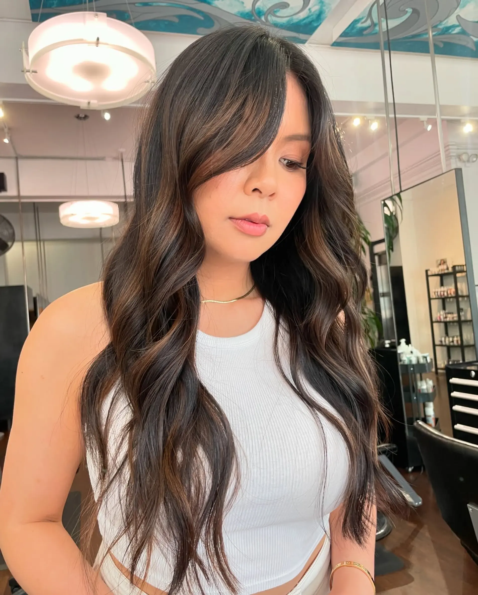 Long chocolate brown hair cut with soft cascading layers and styled into effortless, loose waves with a side-swept fringe. 1