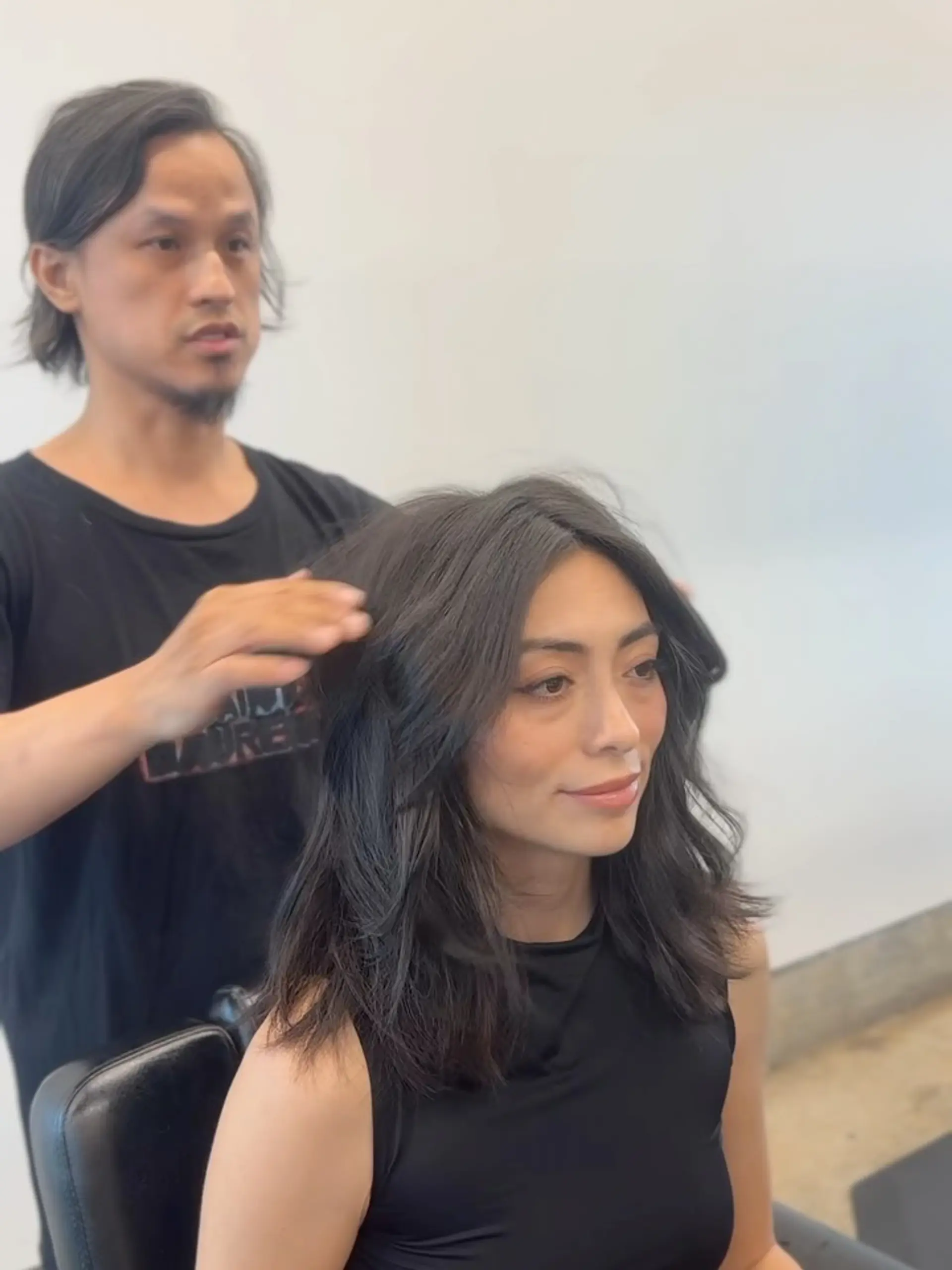 A medium-length dark haircut featuring soft, face-framing layers and curtain bangs styling. 1