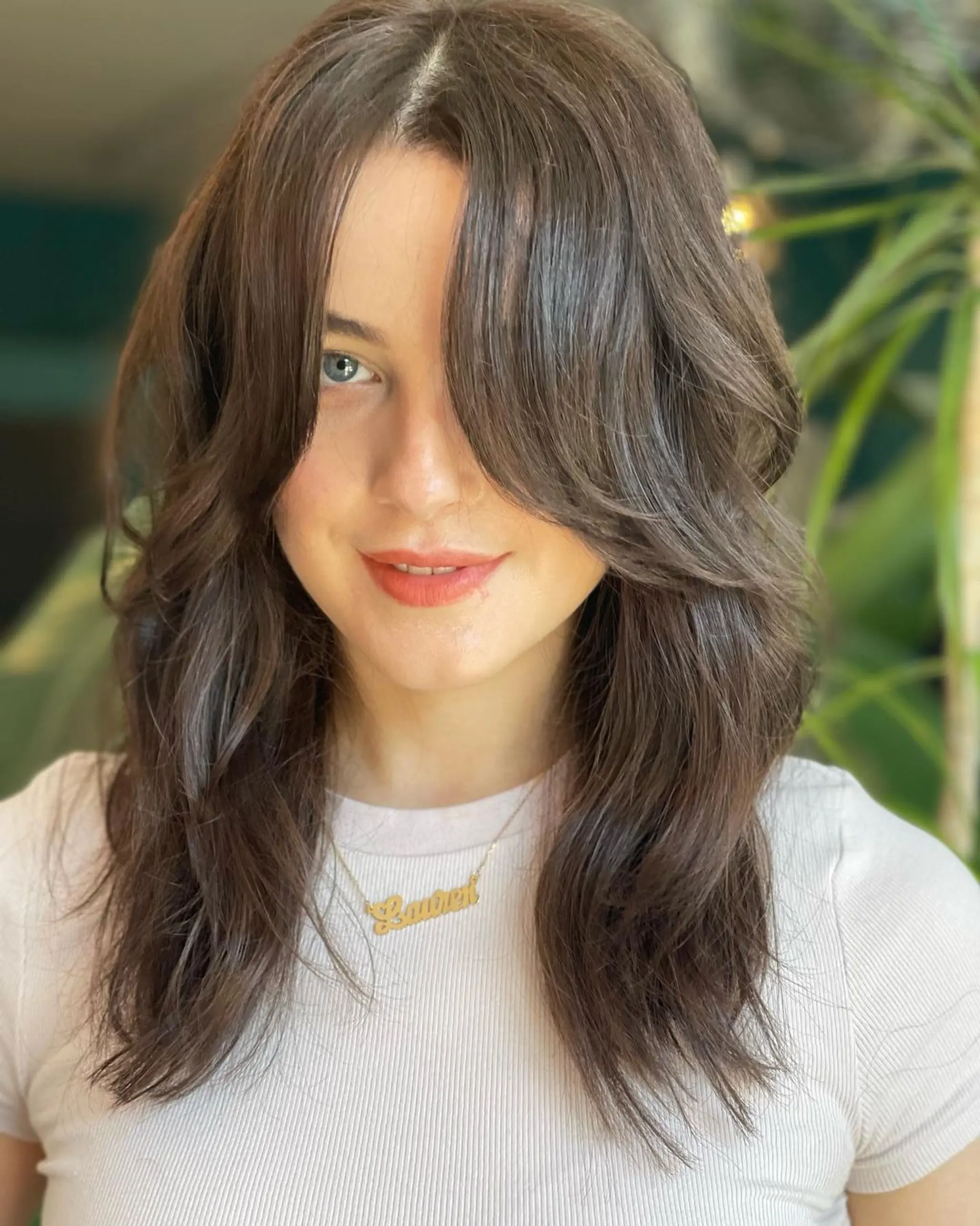 A long, wavy, layered hairstyle with dark brown color featuring elegant curtain bangs and face-framing layers.